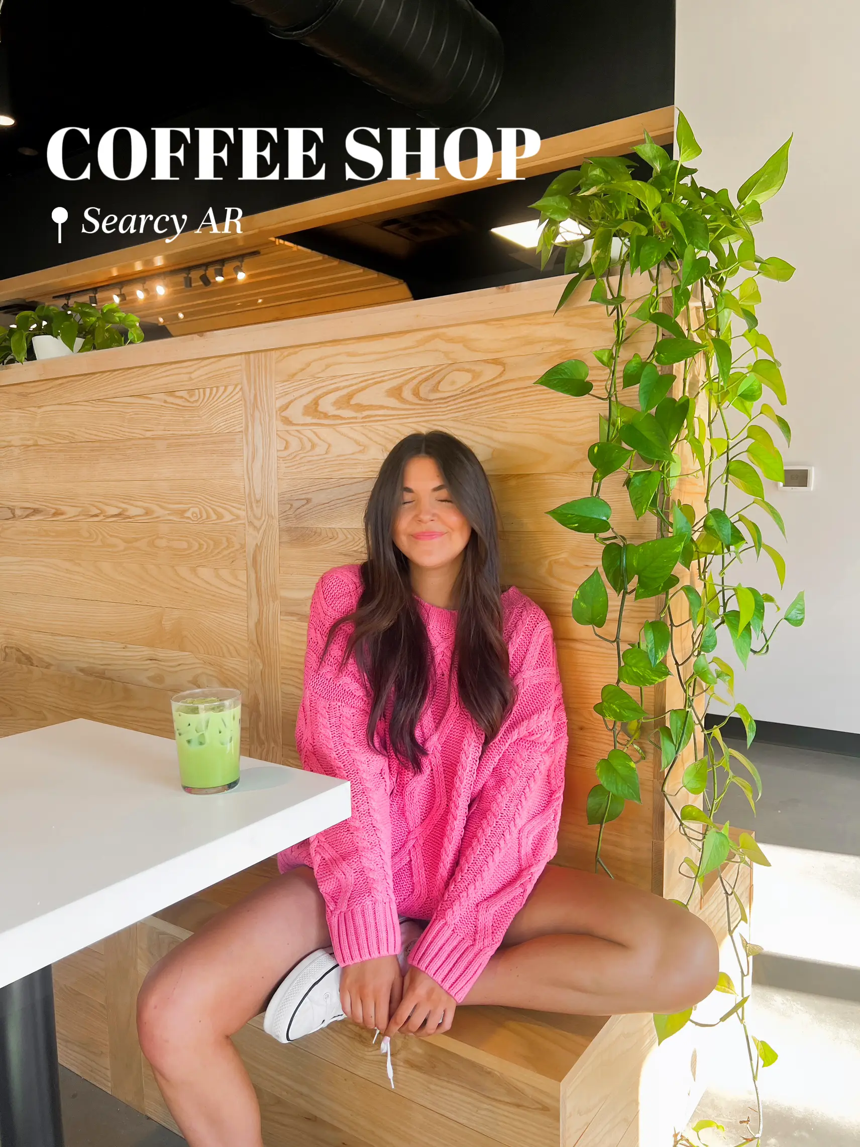  A woman in a pink sweater is sitting on a bench at a coffee shop.