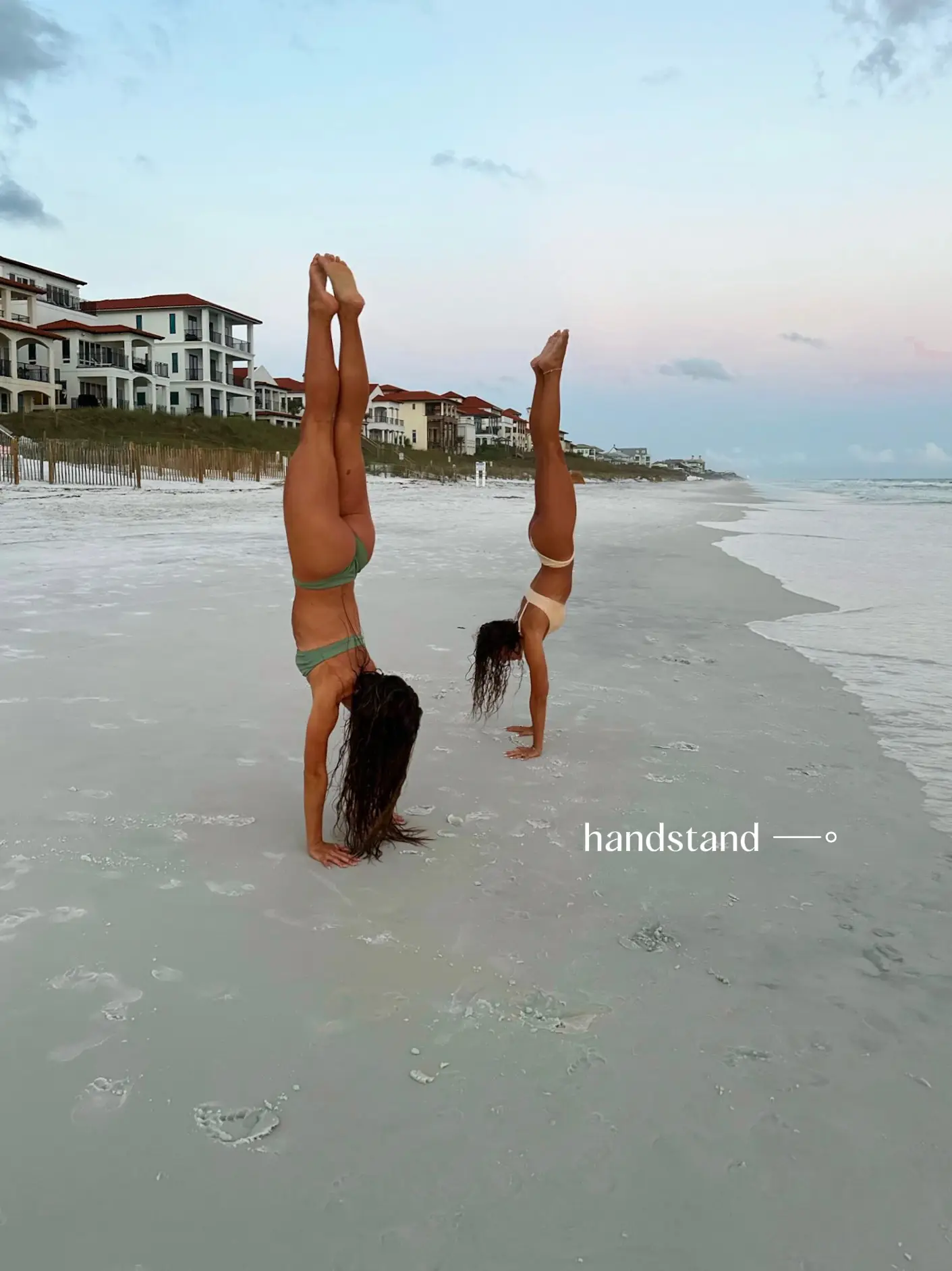  Two women are doing handstands in the ocean.