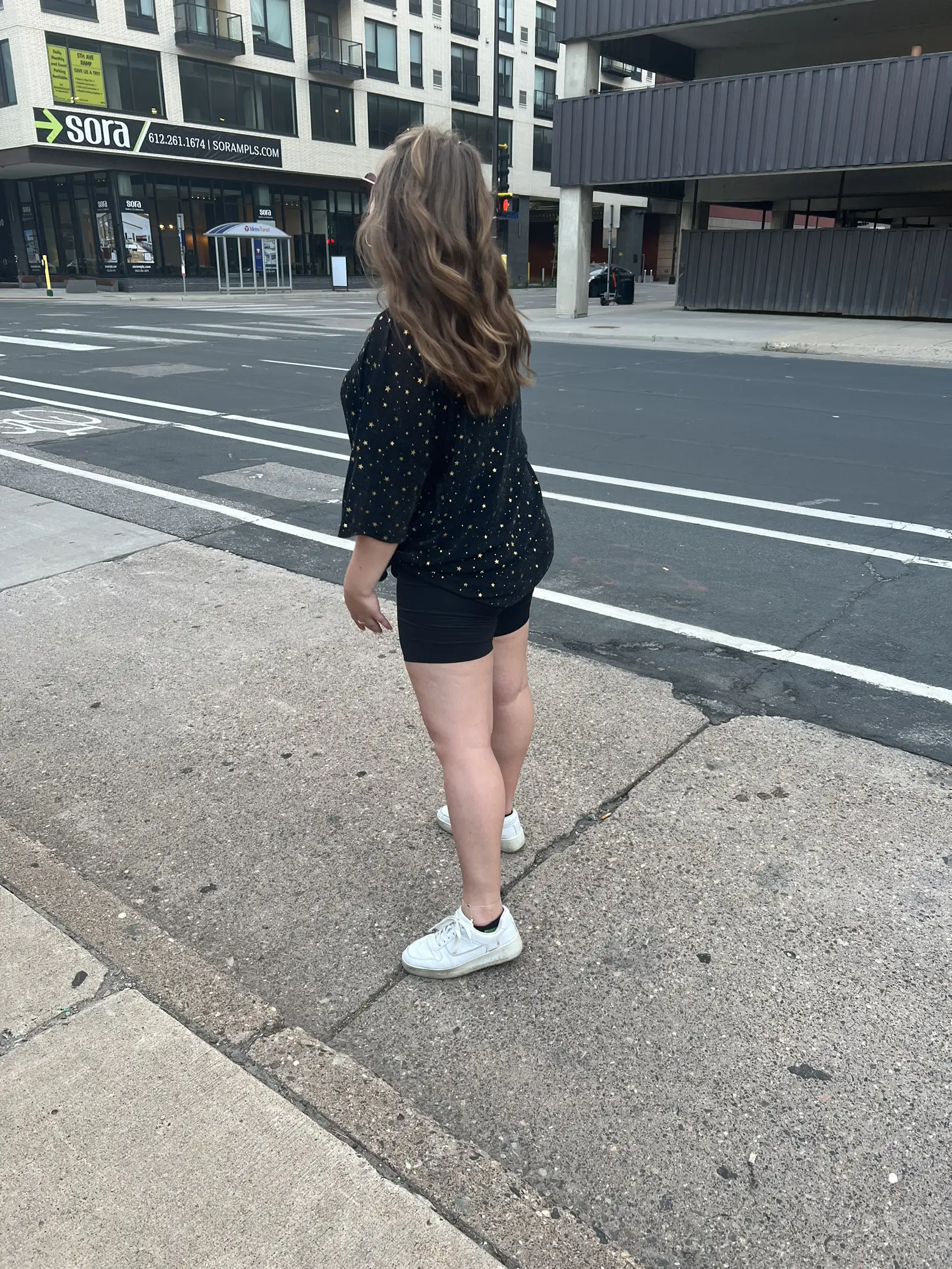  A woman wearing a black shirt and shorts is standing on a sidewalk.