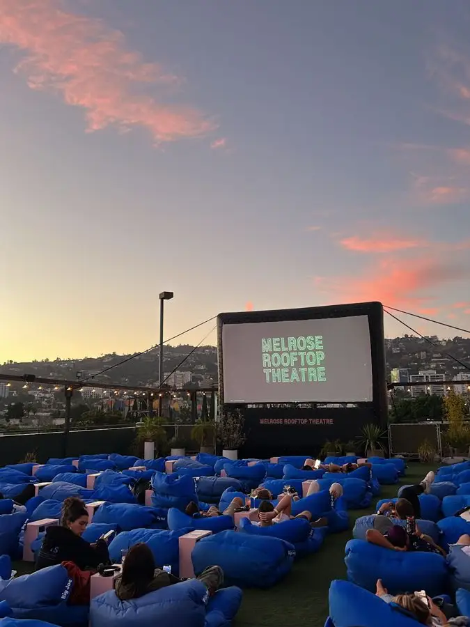  A large group of people are sitting on the grass at the Melrose rooftop theatre.