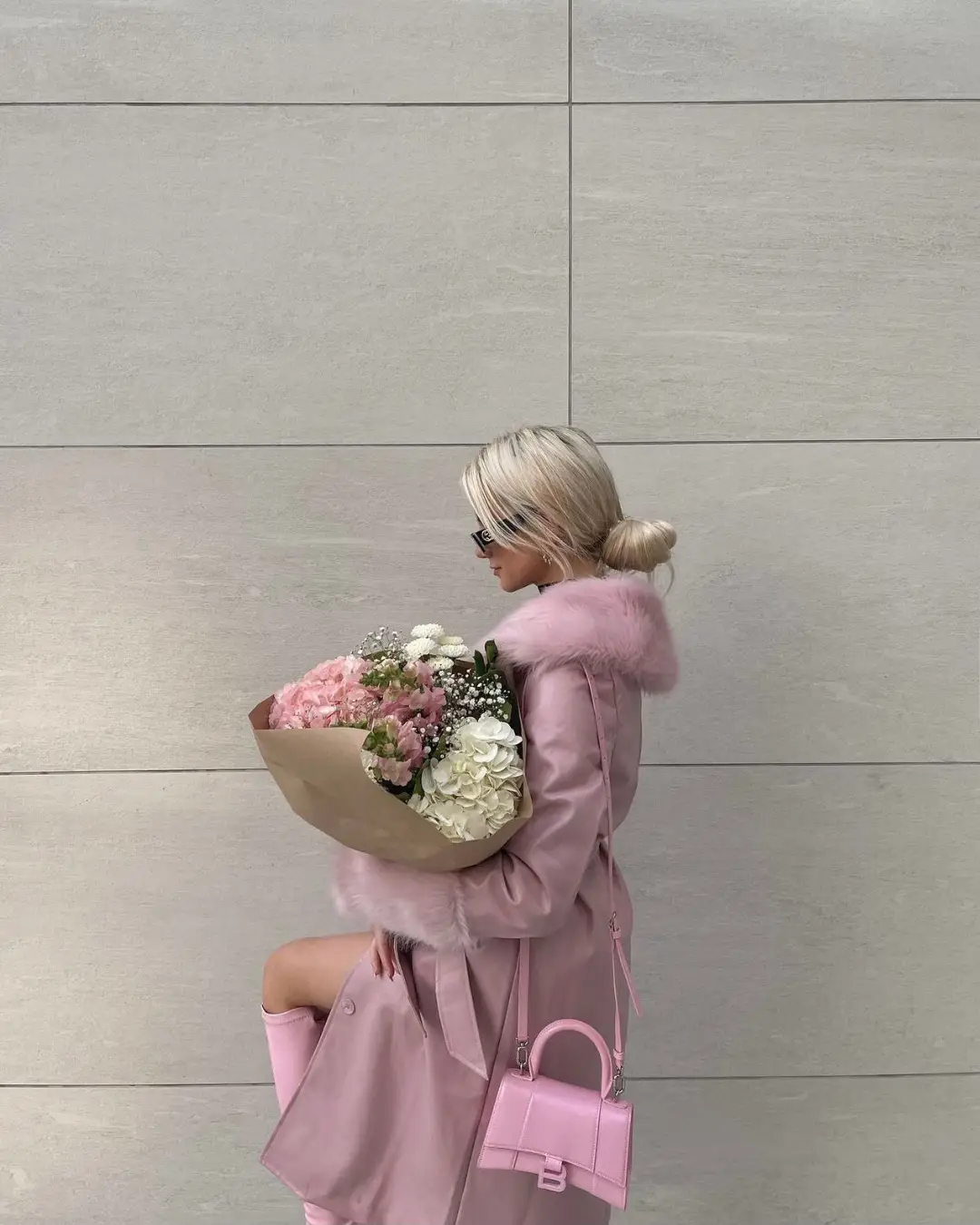  A woman in a pink coat and pink purse is holding a bouquet of flowers.