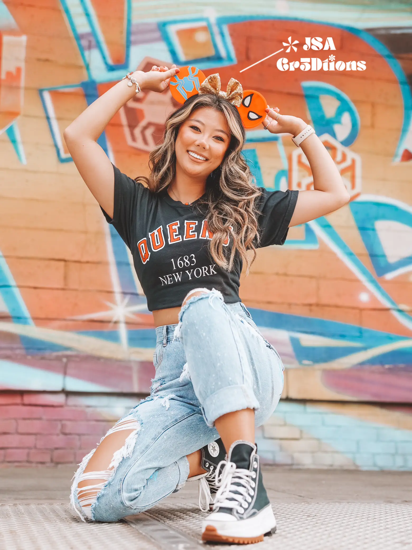  A woman wearing a black shirt with the word New York on it is posing in front of a wall.