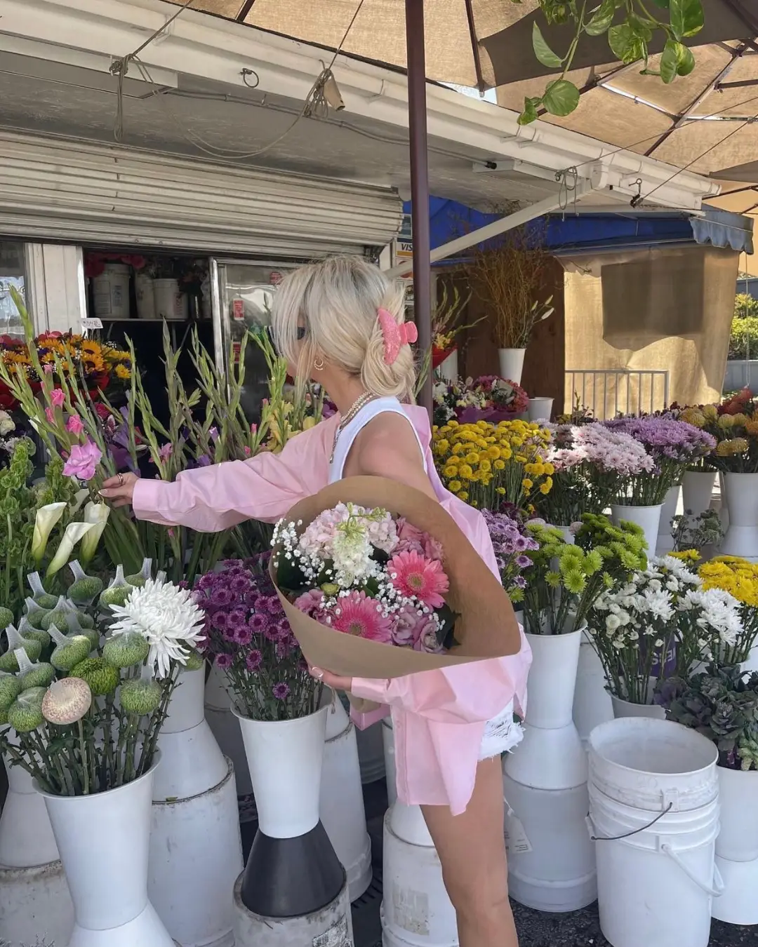  A woman in a pink dress is standing in front of a flower display. She is reaching out to pick flowers from the vases. The vases are filled with flowers and are arranged in a visually appealing manner.