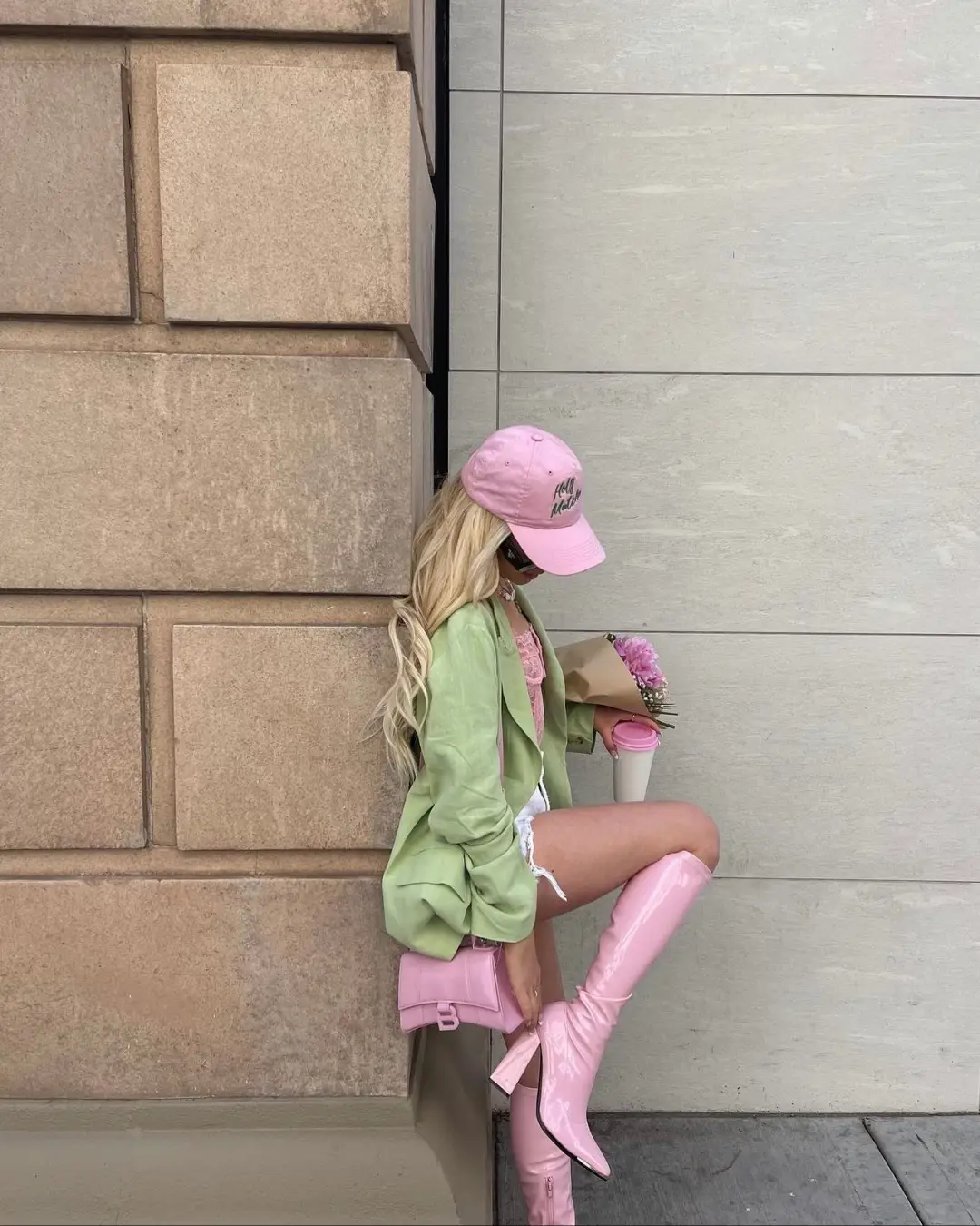  A woman wearing a green jacket and pink pants is sitting on a ledge.