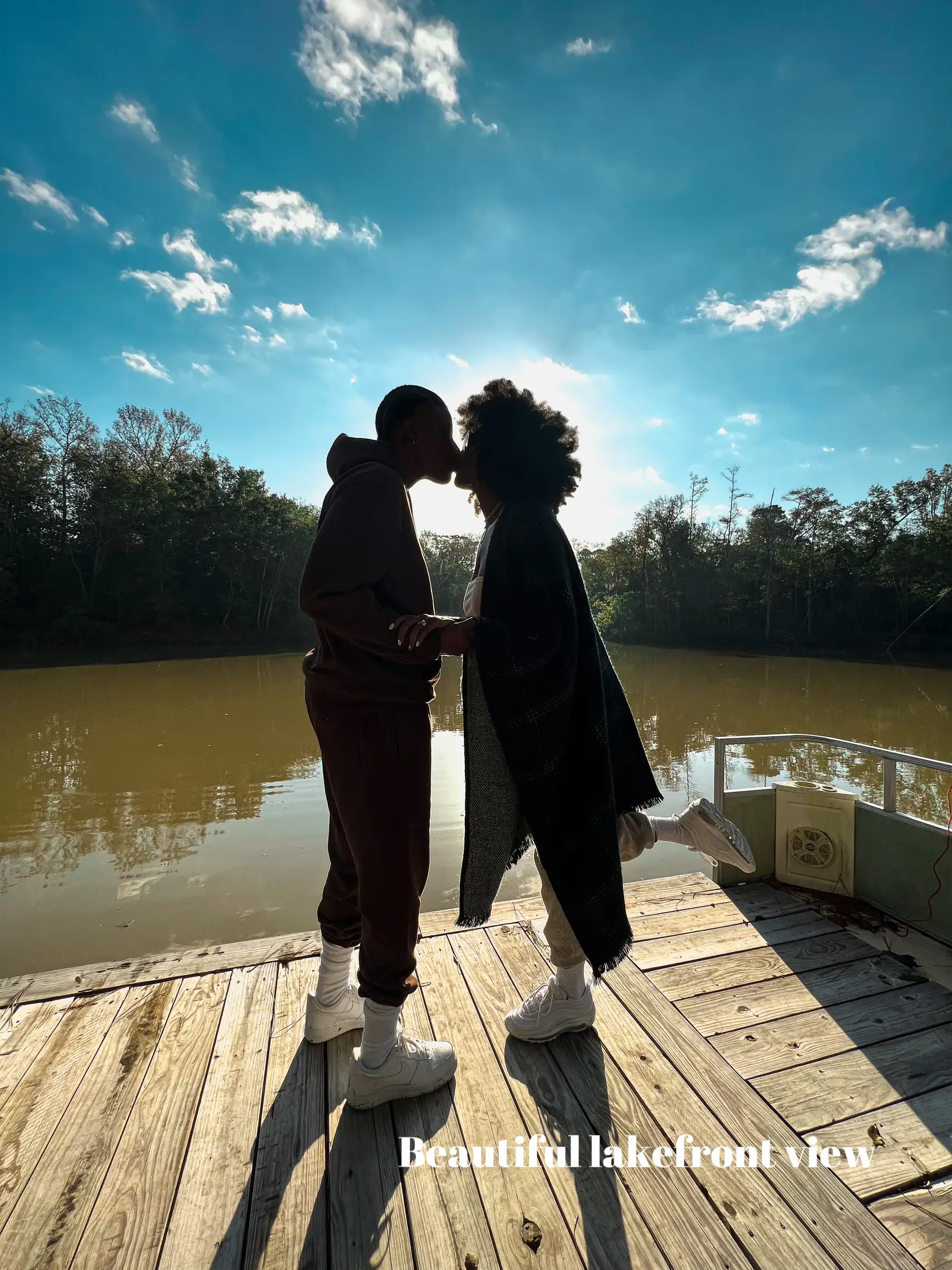  Two people kissing in front of a lake.