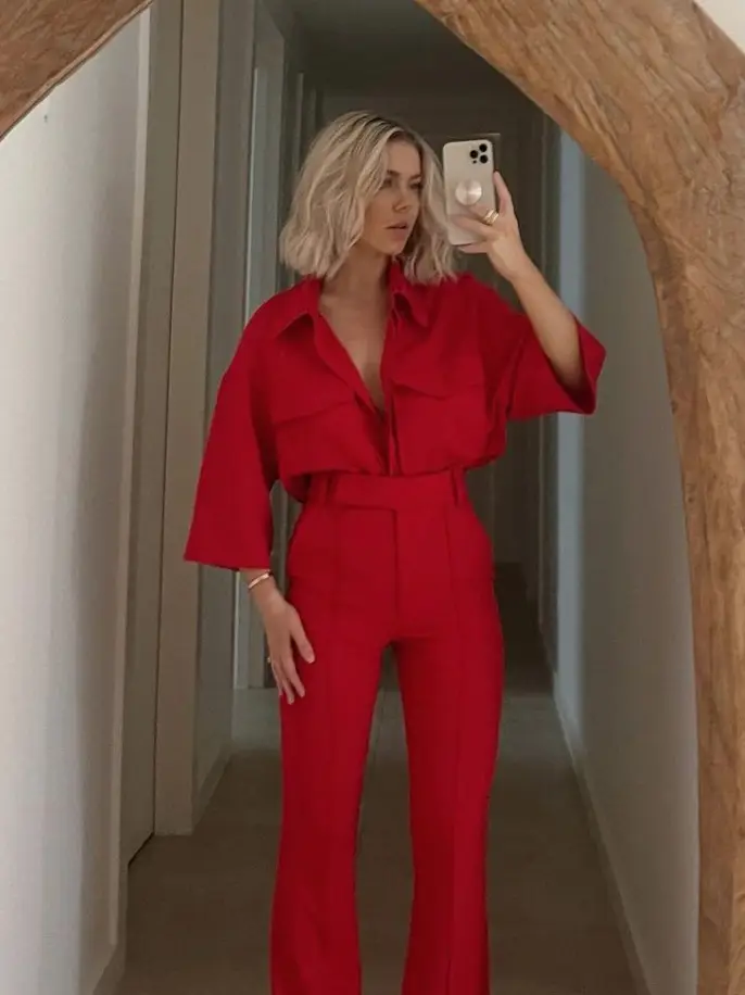  A woman in a red dress is taking a selfie in a hallway.