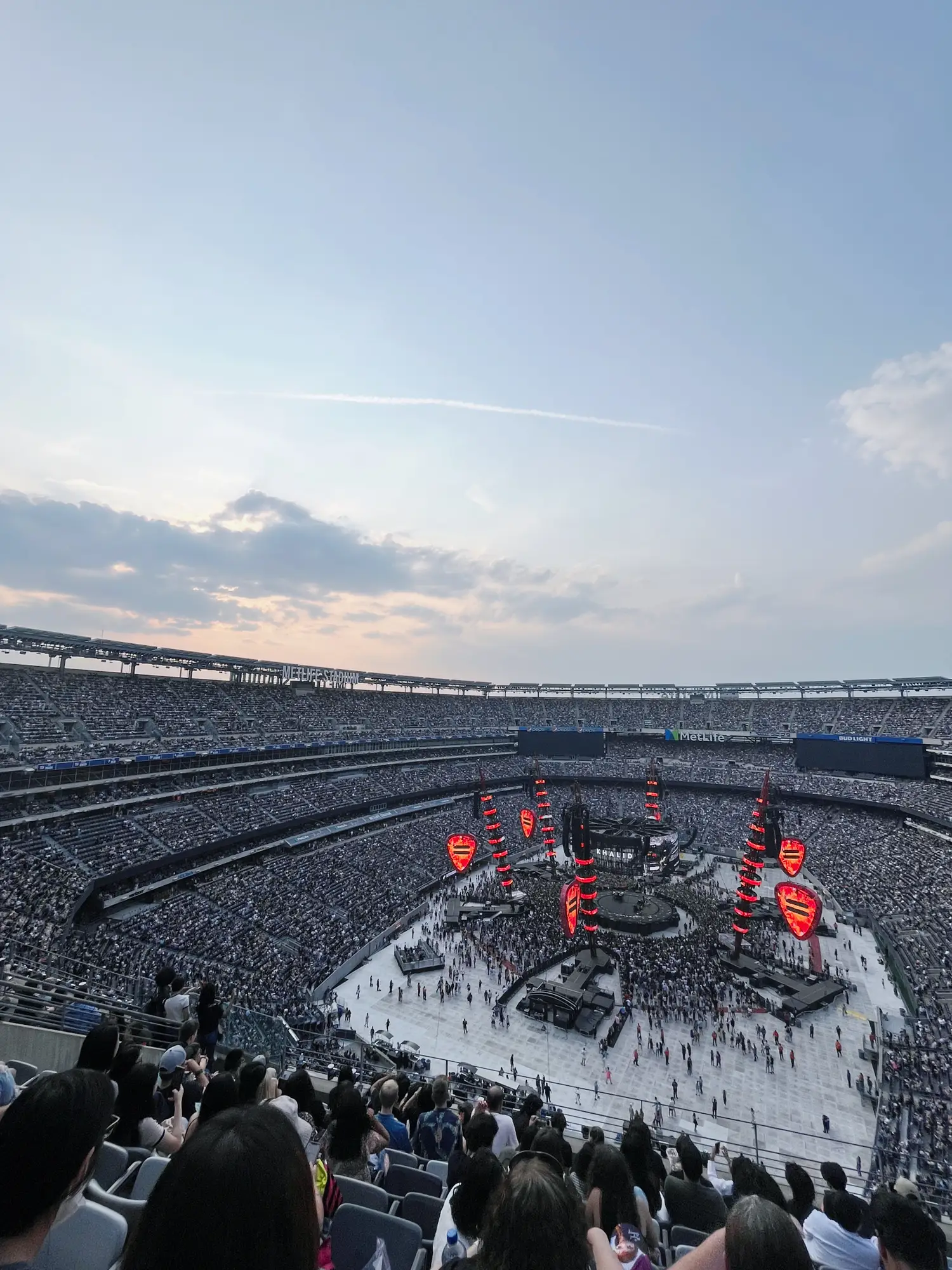  A large crowd of people are gathered in an arena, watching a concert. The audience is seated on chairs and there are several rows of seats. The event is sponsored by Coca Cola and Pepsi. The crowd is engaged in the performance and there are