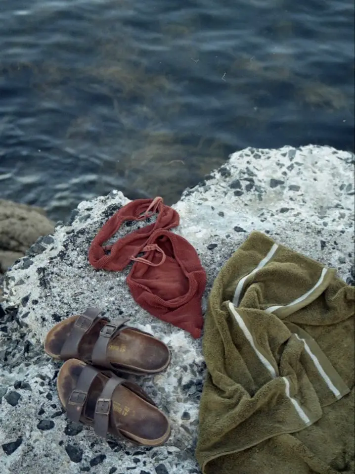 A pair of blue sandals are laying on a rock near the water.
