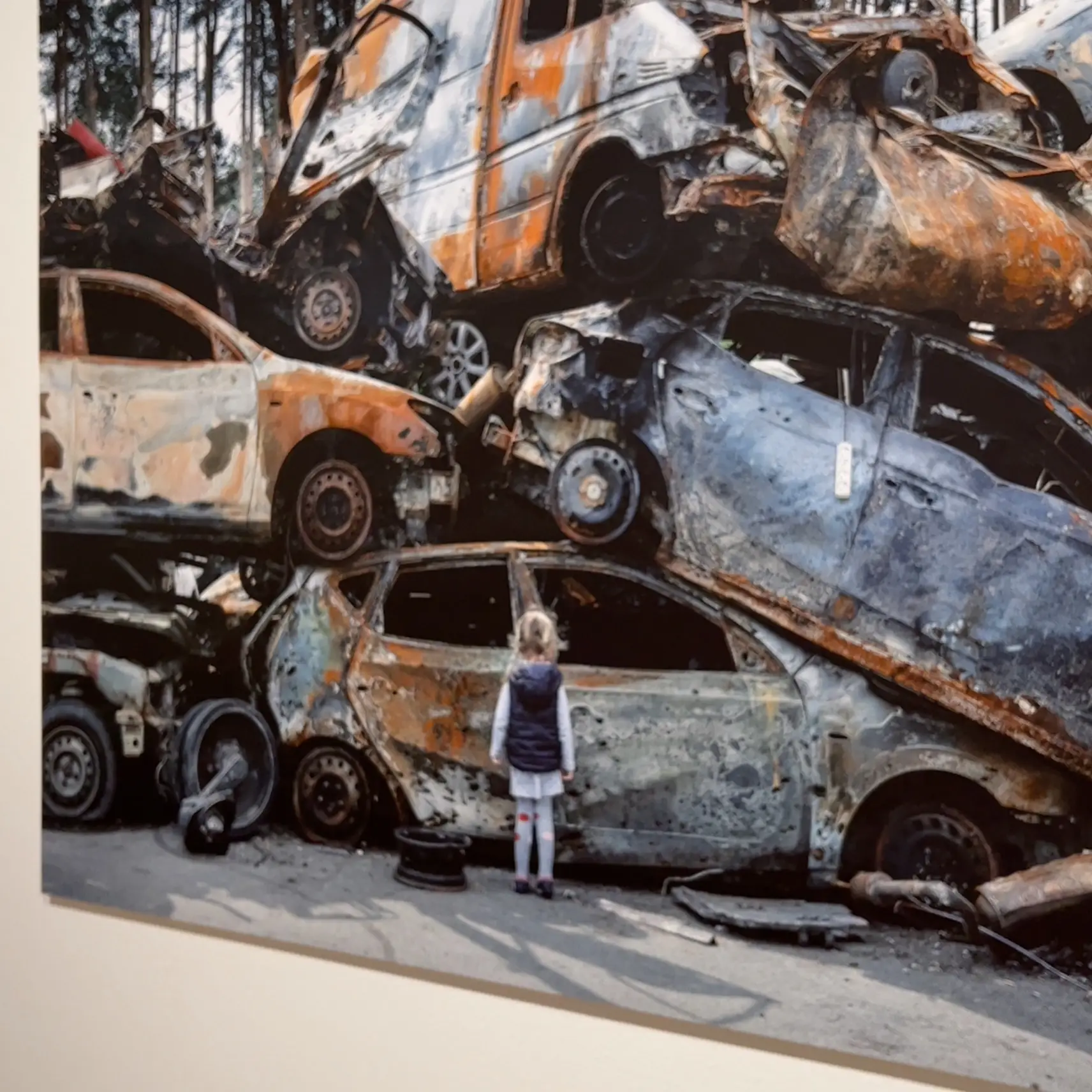  A woman is standing in front of a pile of cars that are crashed and burned.