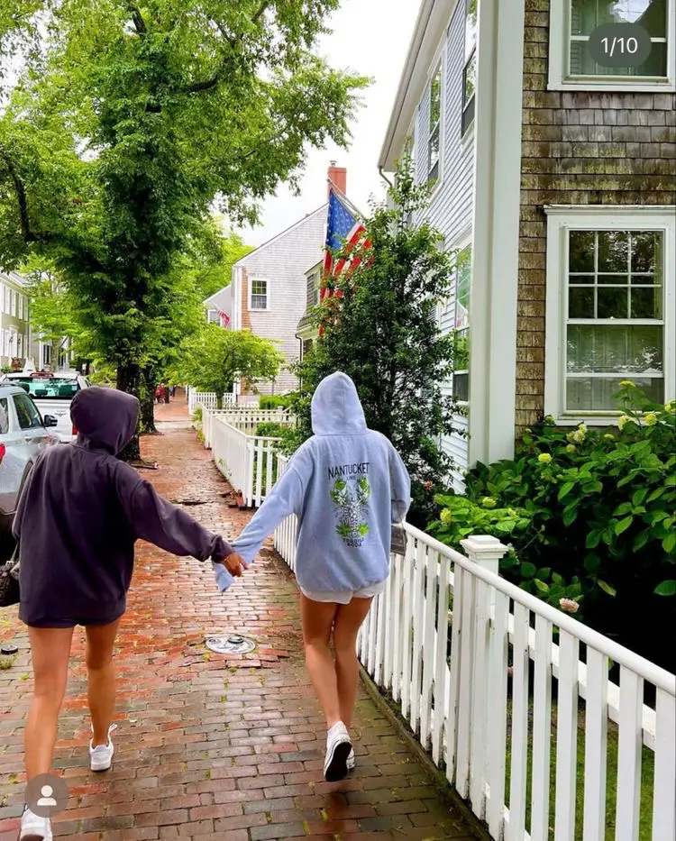  Two women walking down a sidewalk, one wearing a hoodie and the other wearing a hoodie.