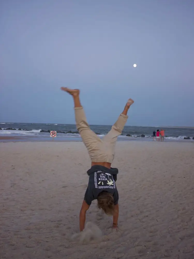  A man is doing a handstand on a towel on the beach.