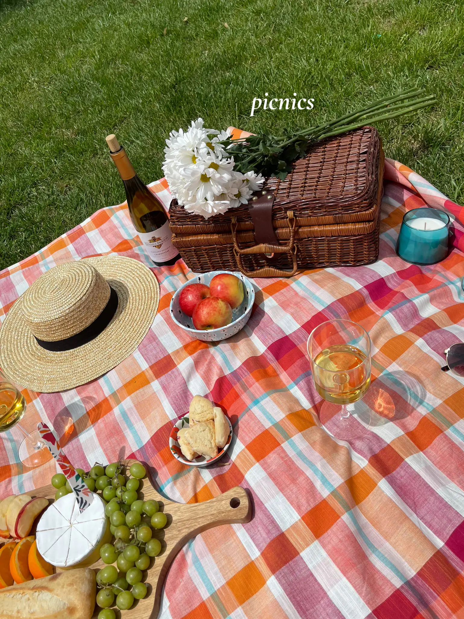  A picnic table with a blue and white checkered tablecloth and a basket of fruit on it.