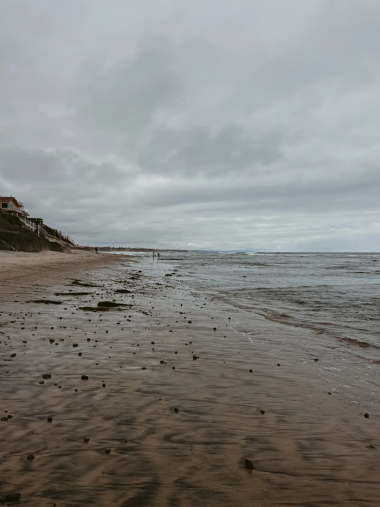 A beach scene with a house in the background and a cloudy sky.