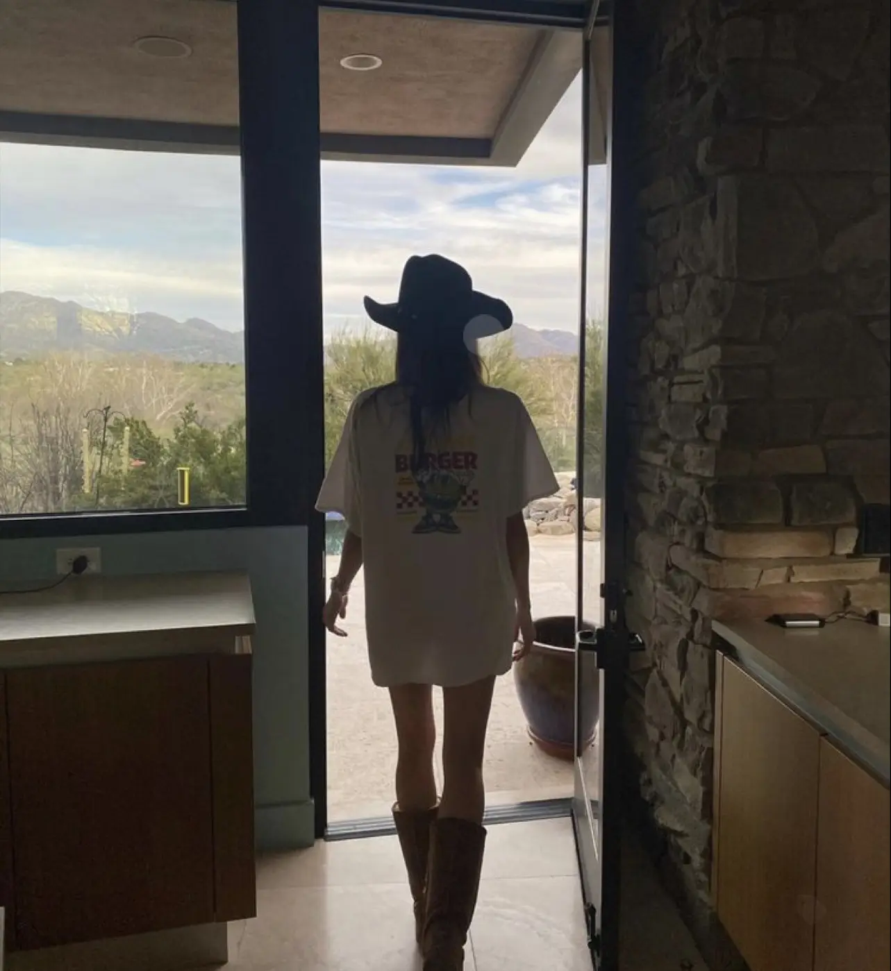  A woman wearing a white shirt and cowboy boots is standing in a kitchen.
