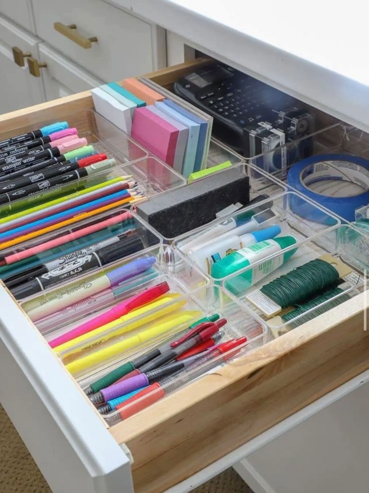  A drawer with a white desk and a variety of office supplies inside.