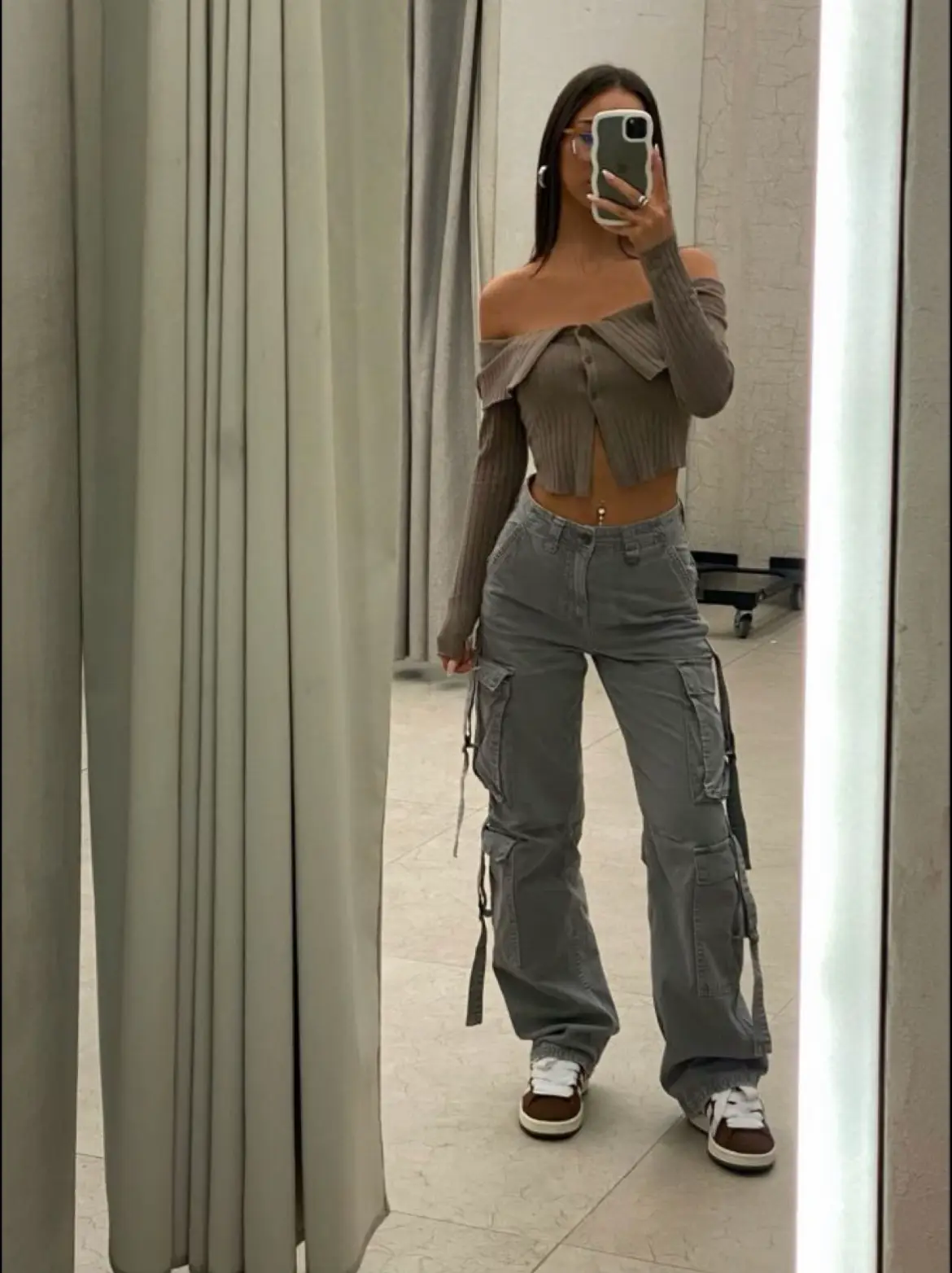  A woman wearing a white shirt and jeans is taking a selfie in a mirror.