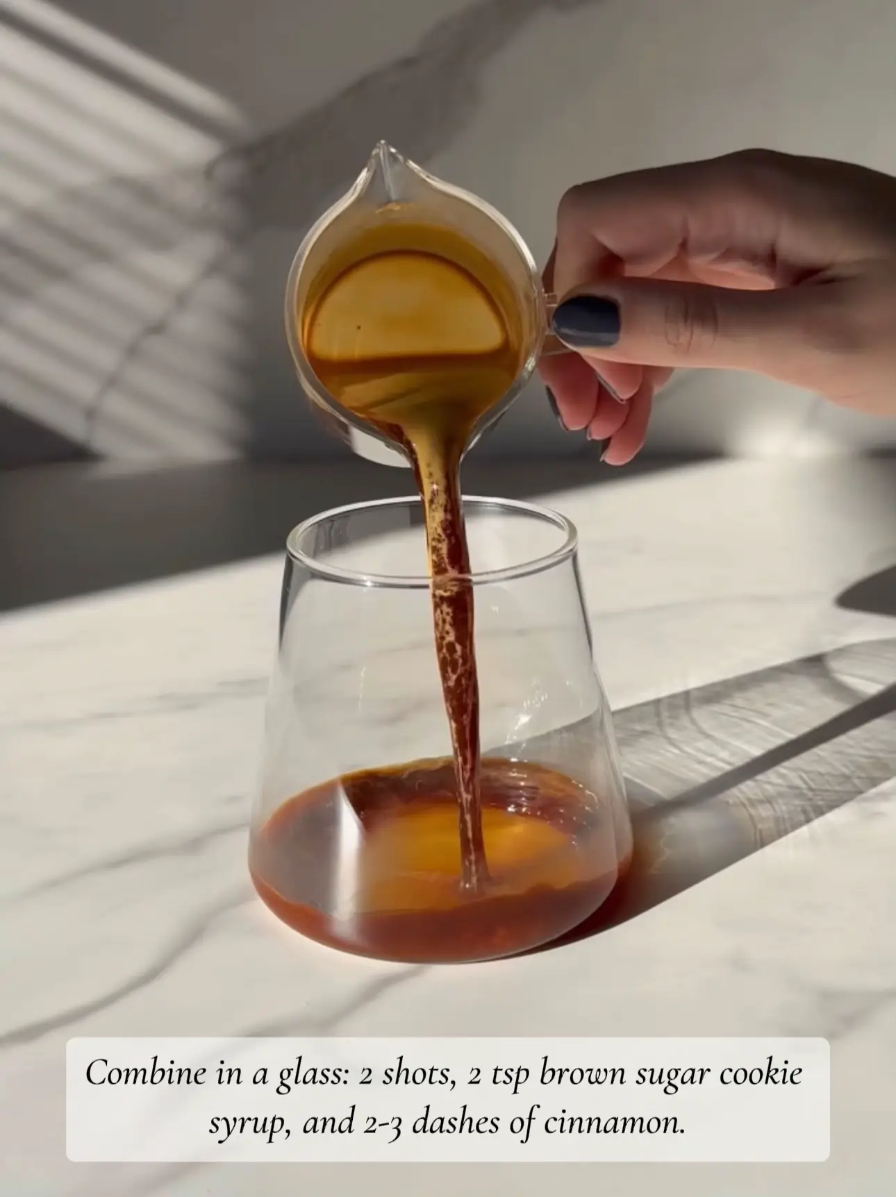  A person is holding a glass with a spoon in it. The glass contains brown sugar cookie syrup and cinnamon