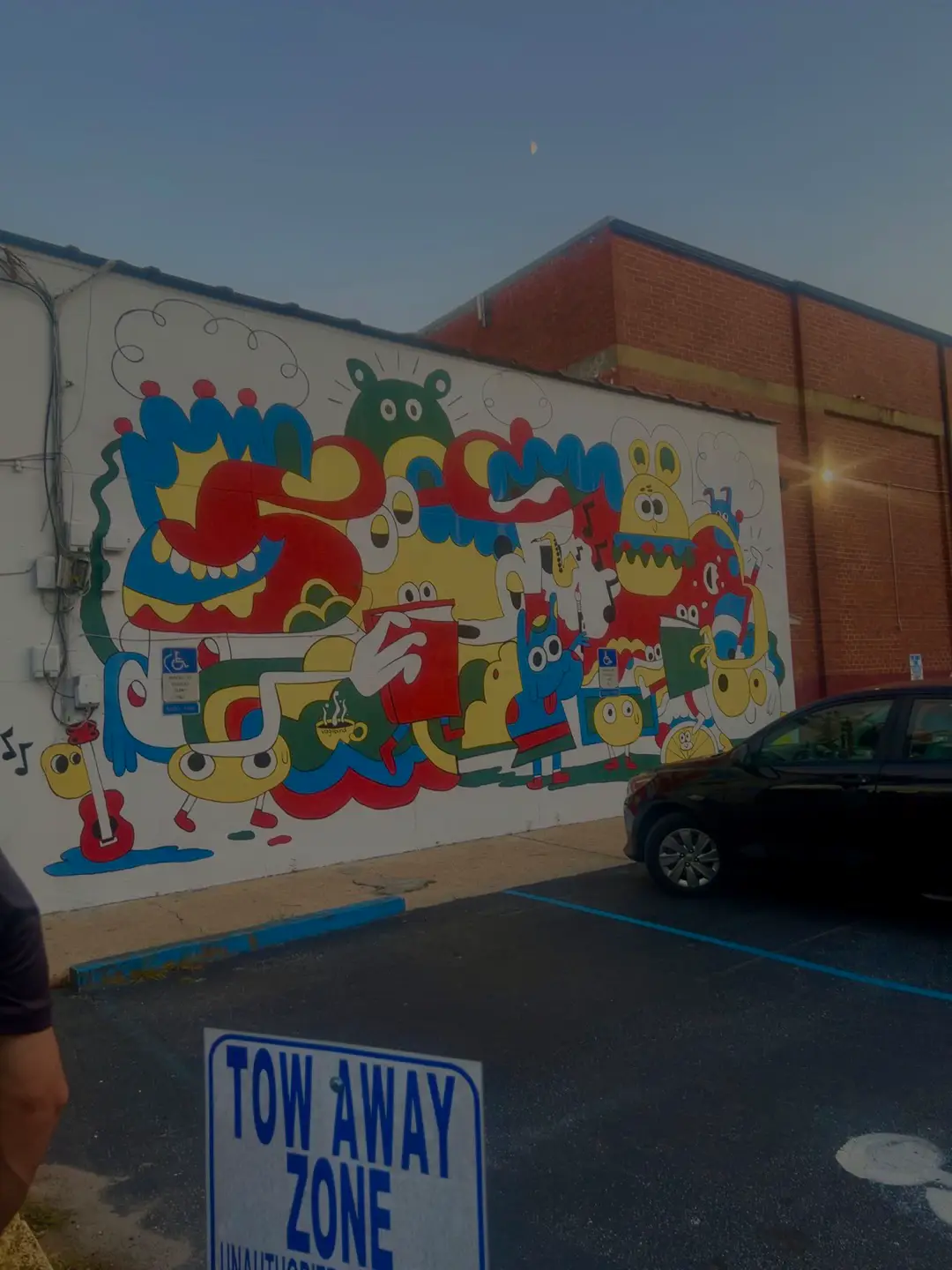  A parking lot with a wall covered in colorful drawings of animals. A sign that says towing zone.