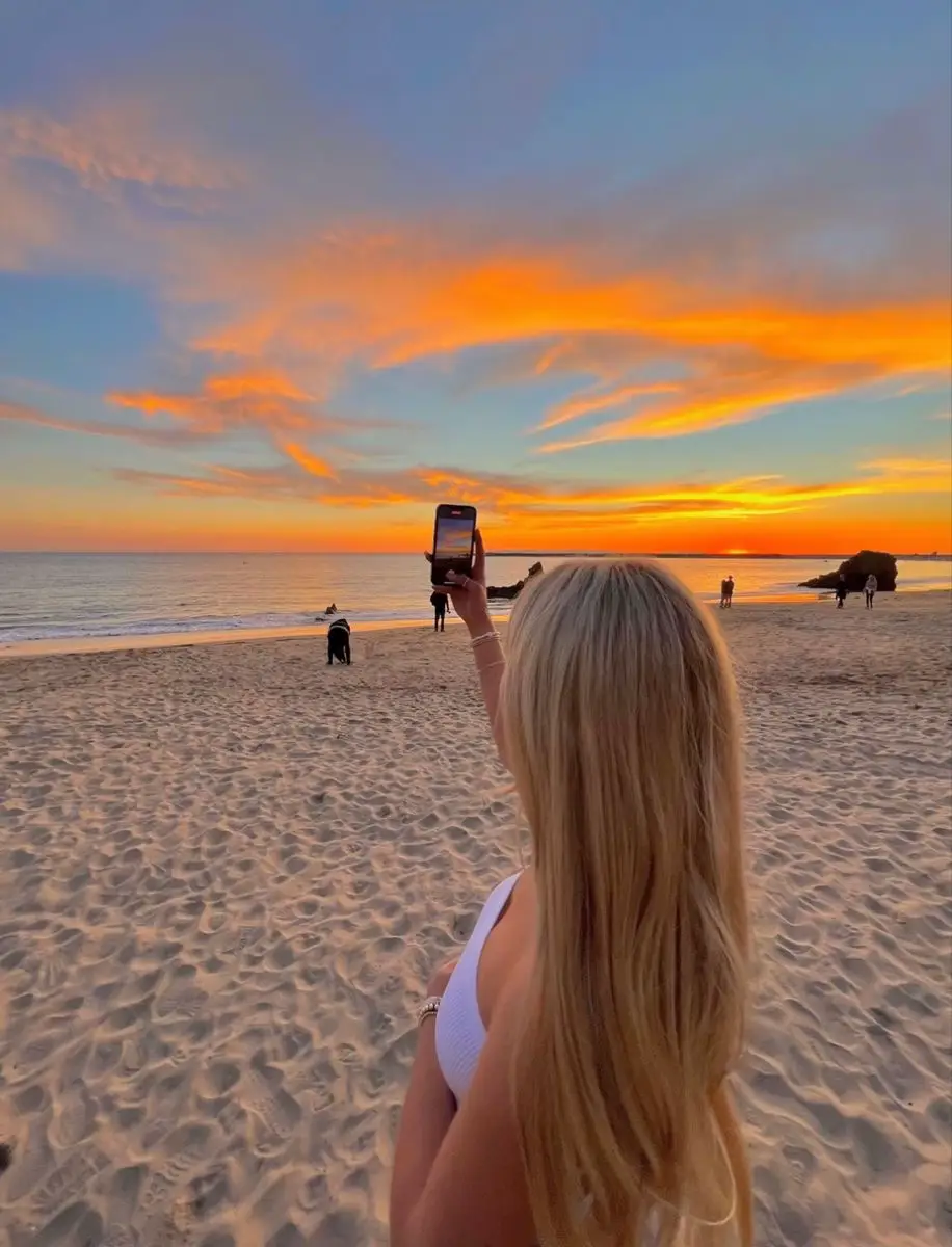  A woman with blonde hair is taking a selfie on a beach.