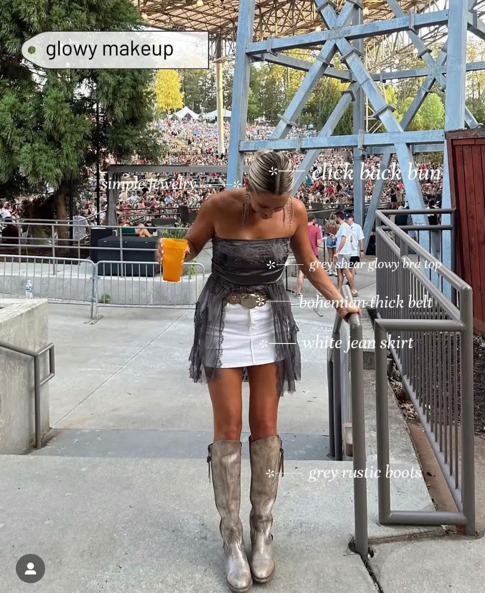  A woman wearing a grey dress and grey boots is standing in front of a fence.