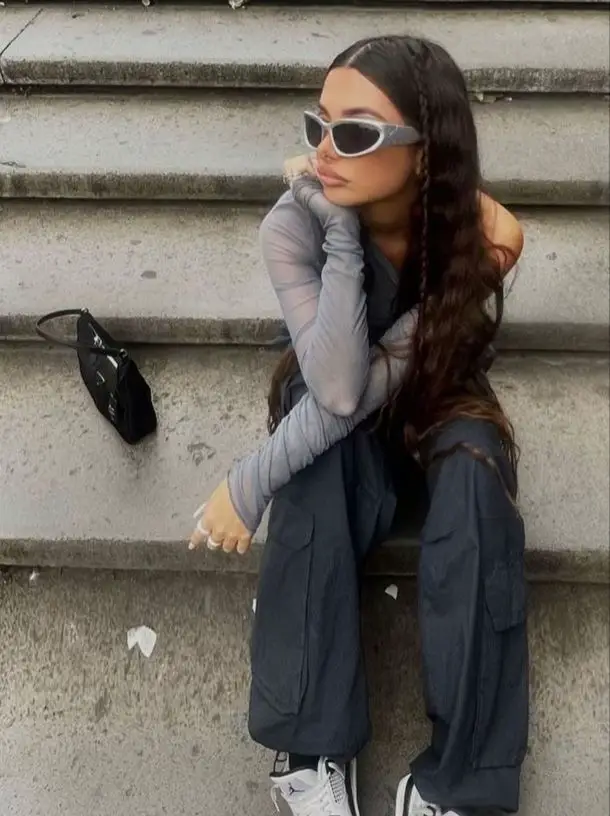 A woman wearing sunglasses and a grey shirt is sitting on a staircase.