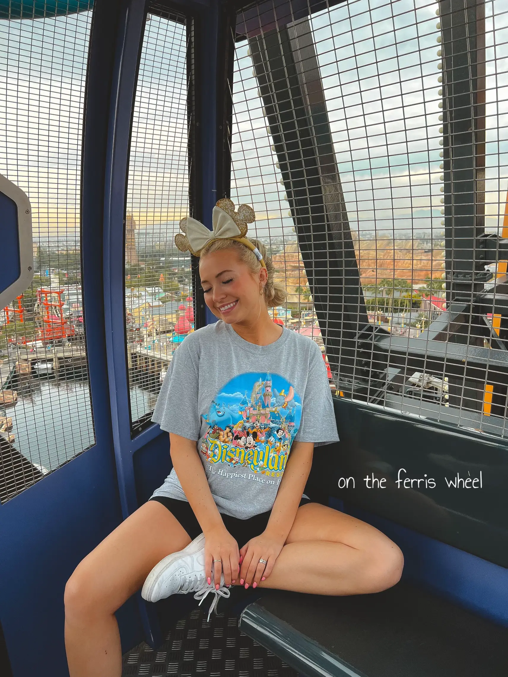  A woman wearing a white shirt and black shorts is sitting on a ferris wheel.