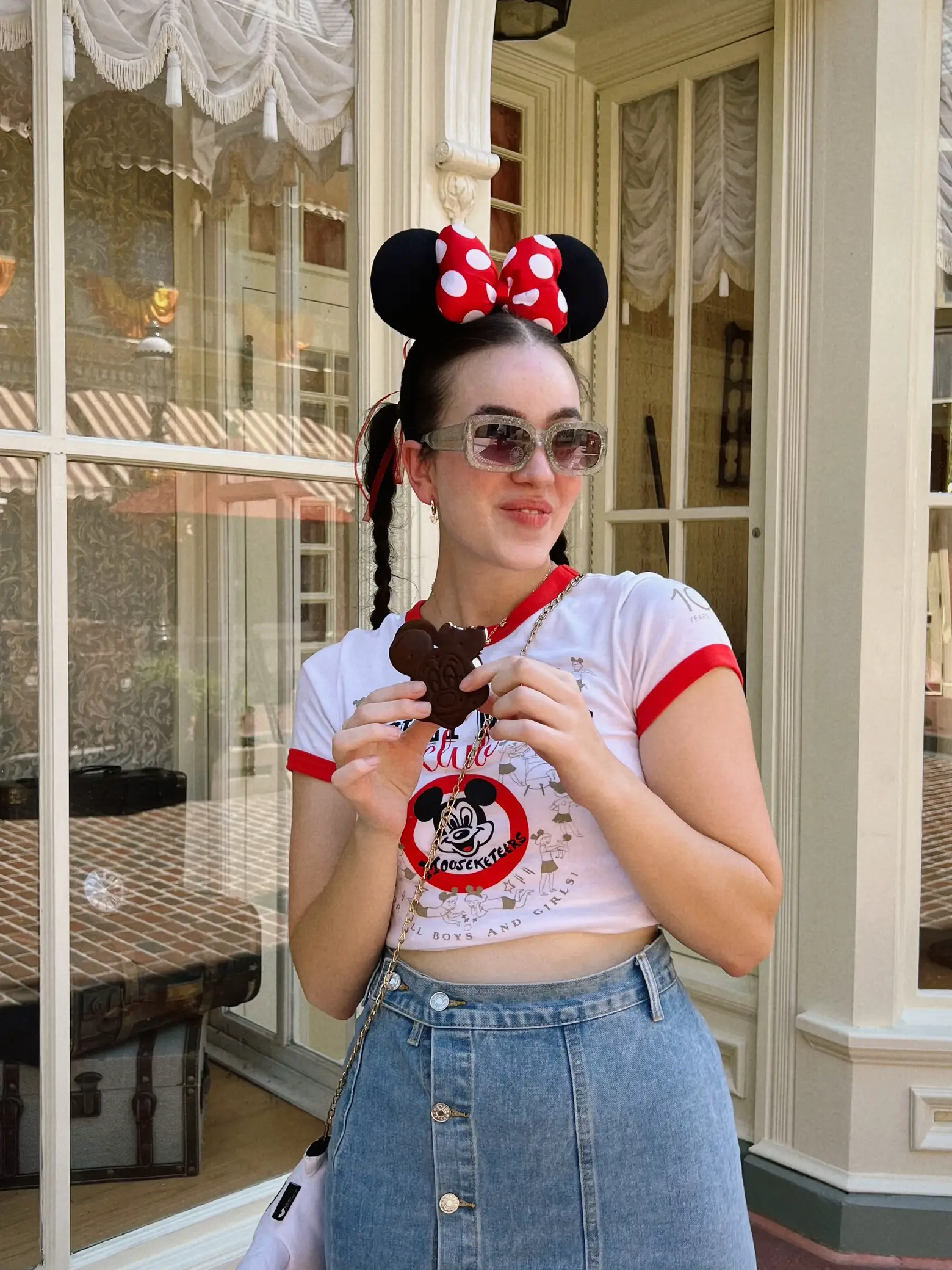  A woman wearing a Mickey Mouse shirt and jeans is holding a piece of chocolate cake.