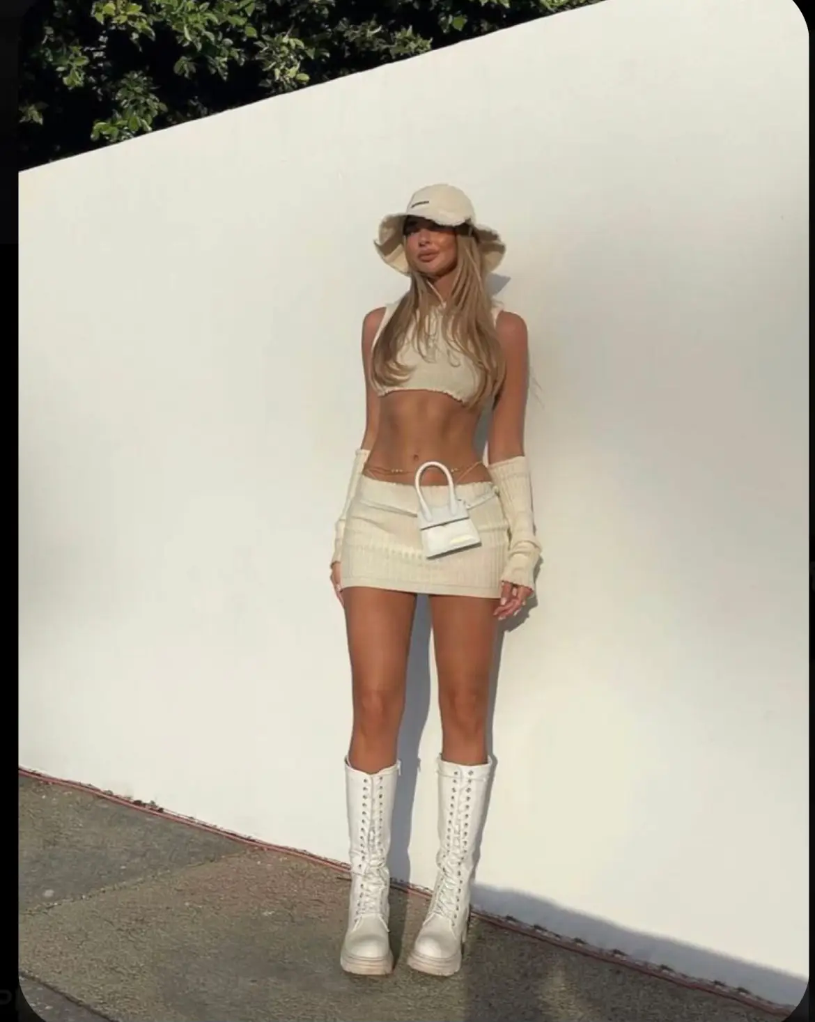  A woman wearing a white hat and white shorts stands in front of a wall.