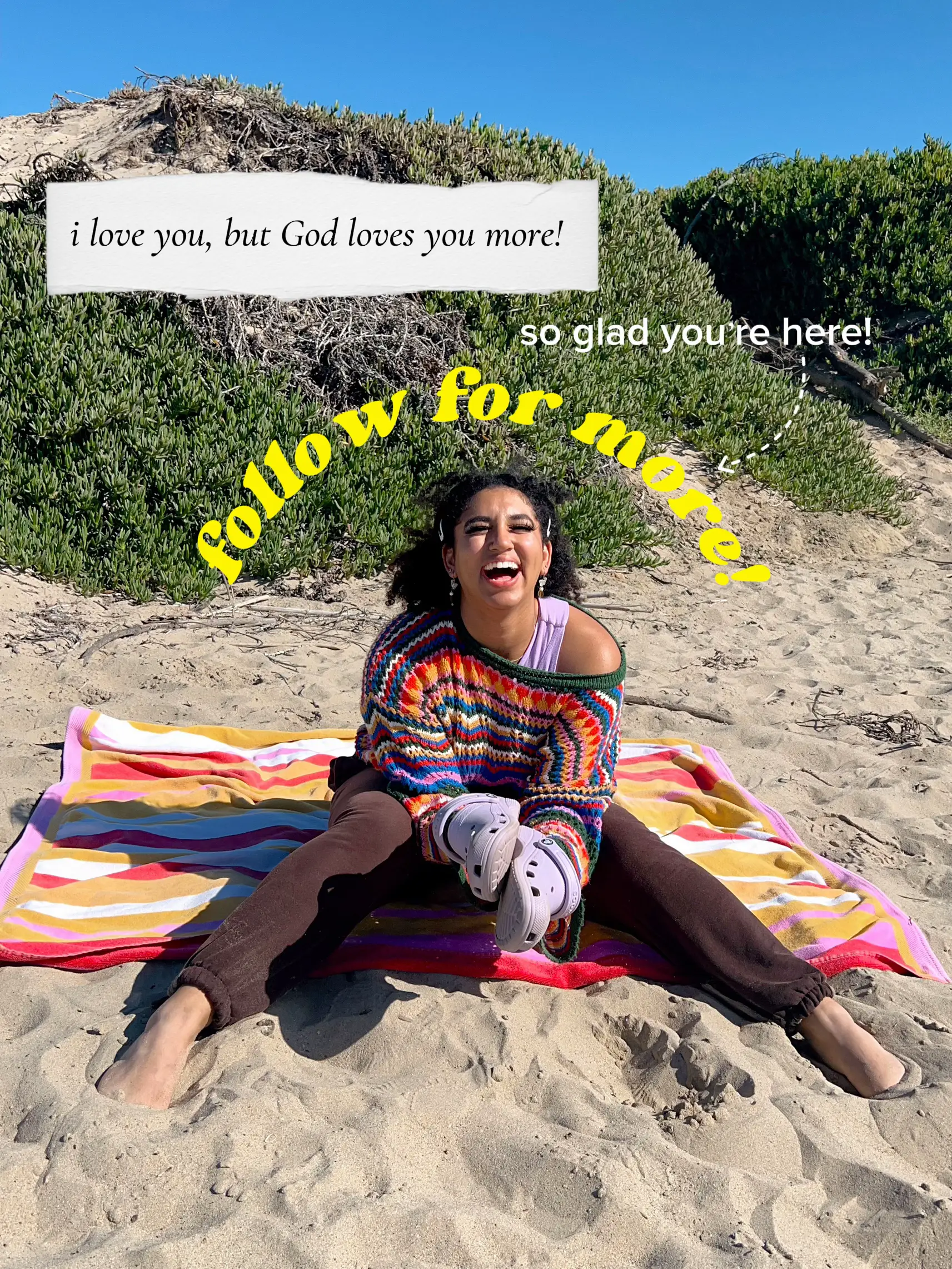  A woman is sitting on a blanket on the beach, and she is wearing a colorful sweater.