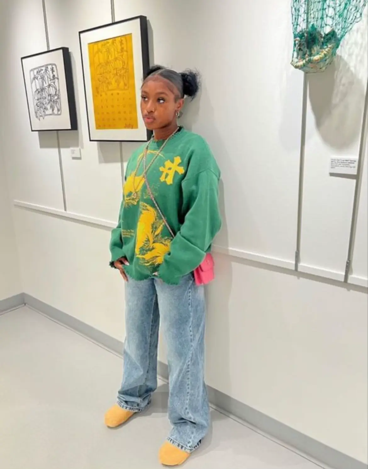  A woman wearing a green sweatshirt and blue jeans stands in a room.