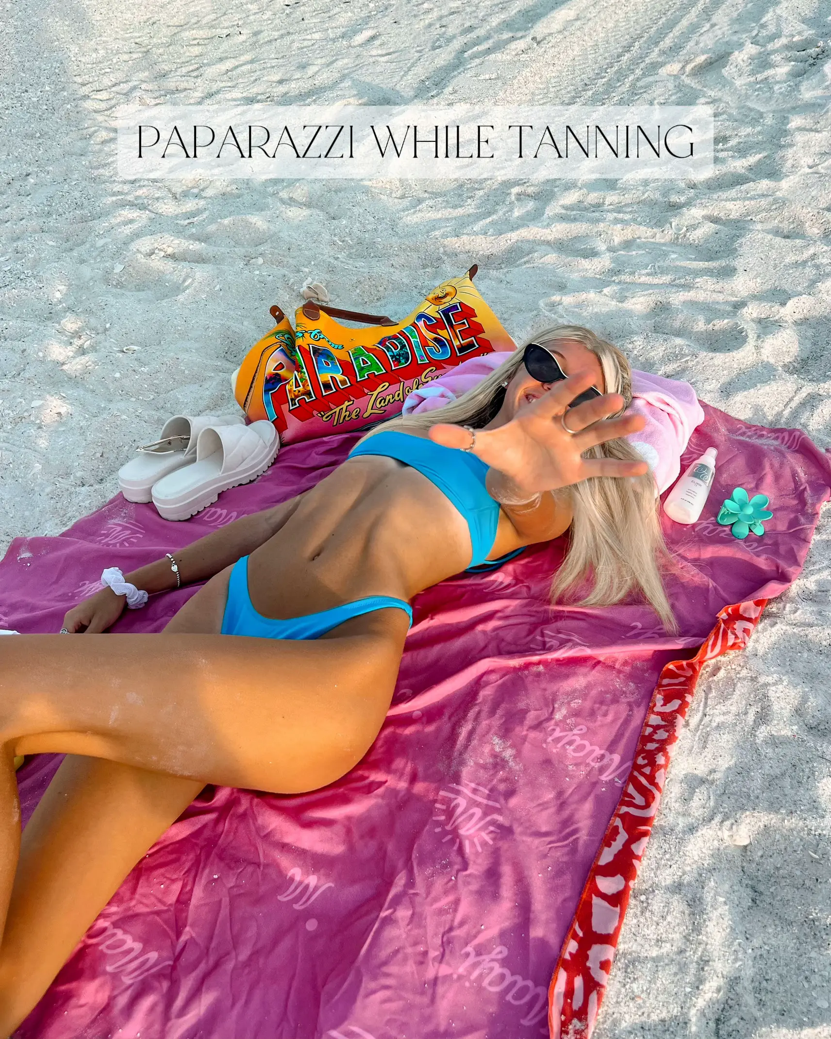  A woman is laying on a pink and white towel on the beach.