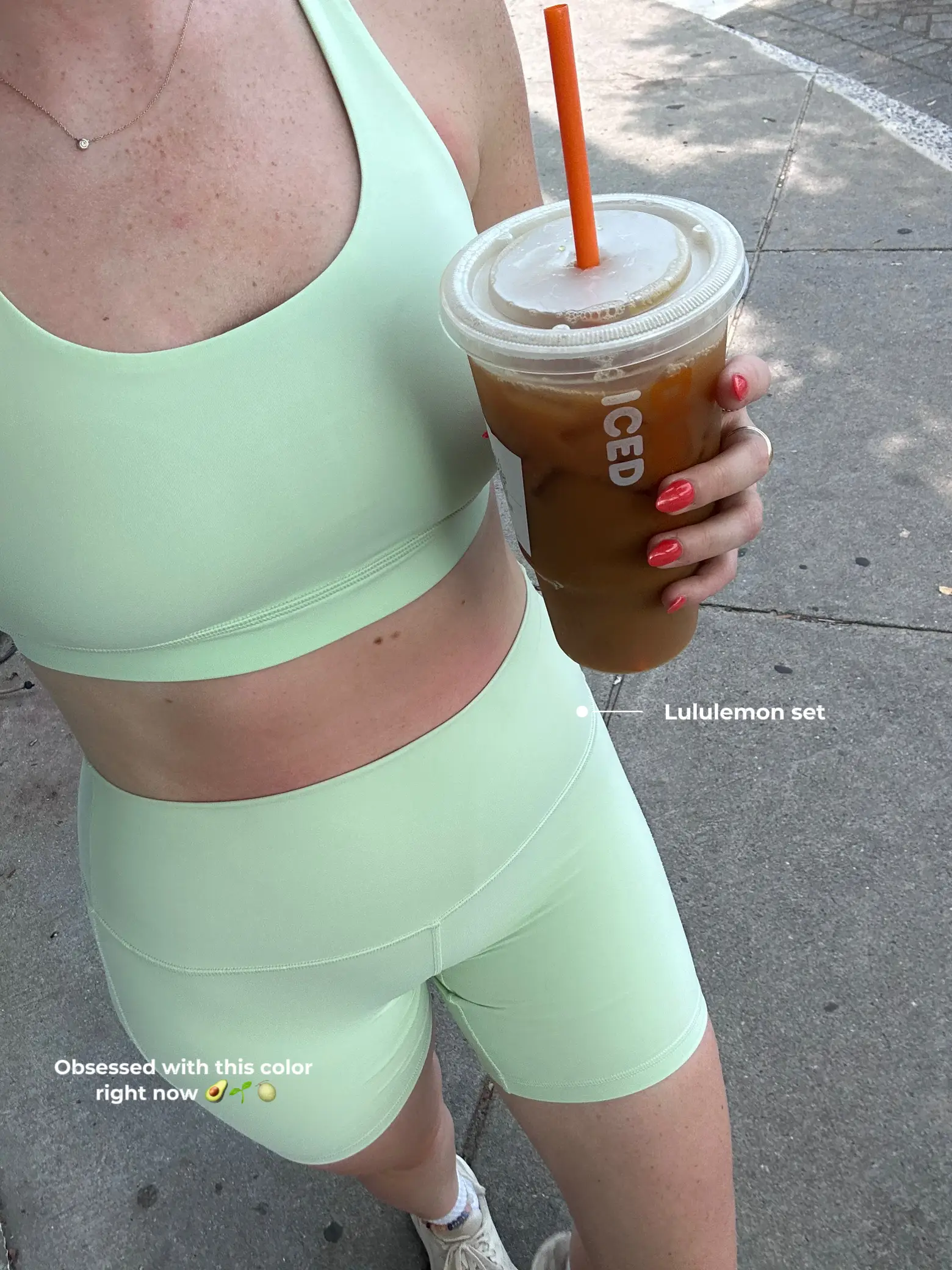 A woman wearing a green Lululemon set is holding a cup of iced coffee.