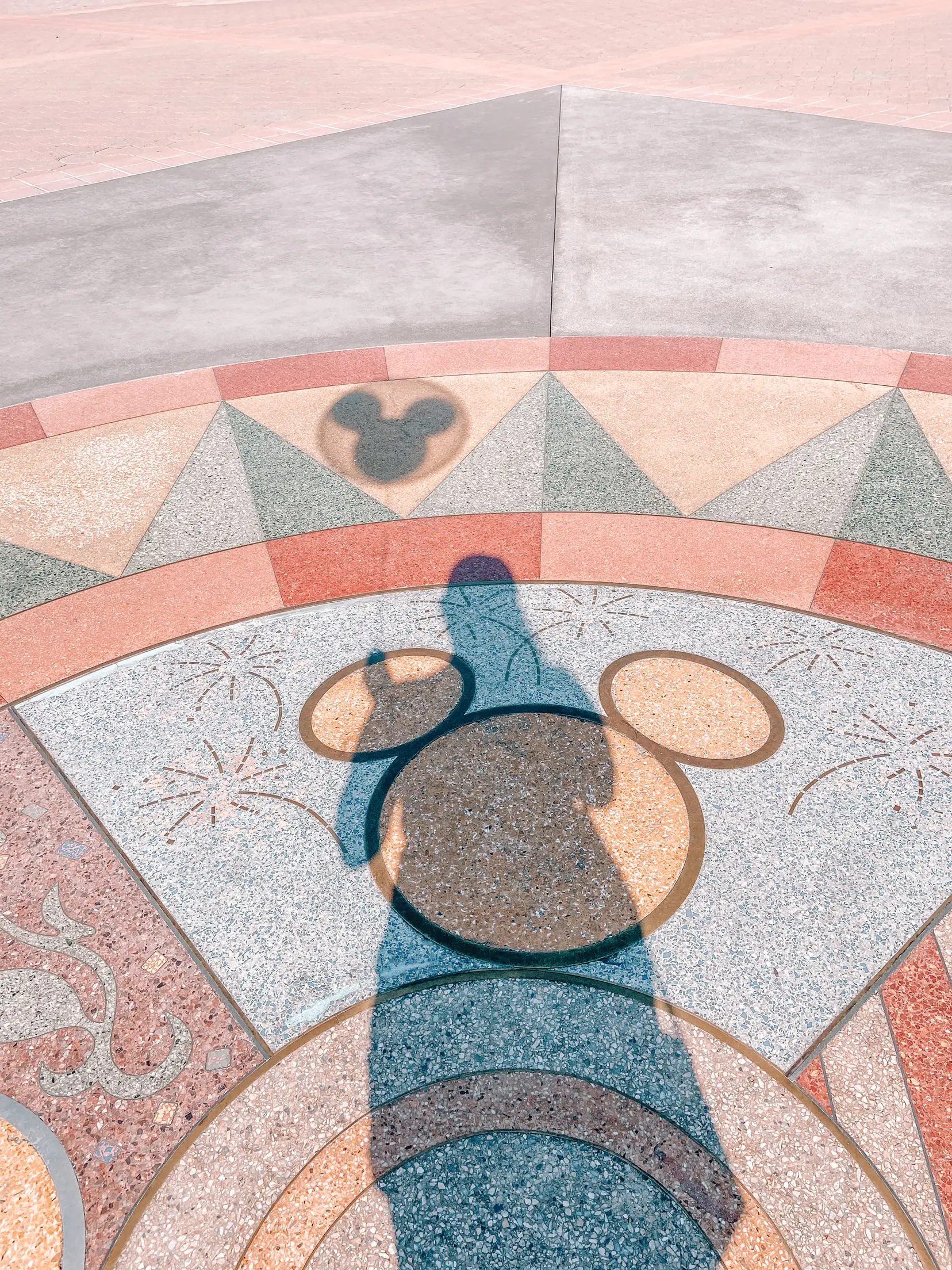  A person is walking on a tile floor with a Mickey Mouse shadow.