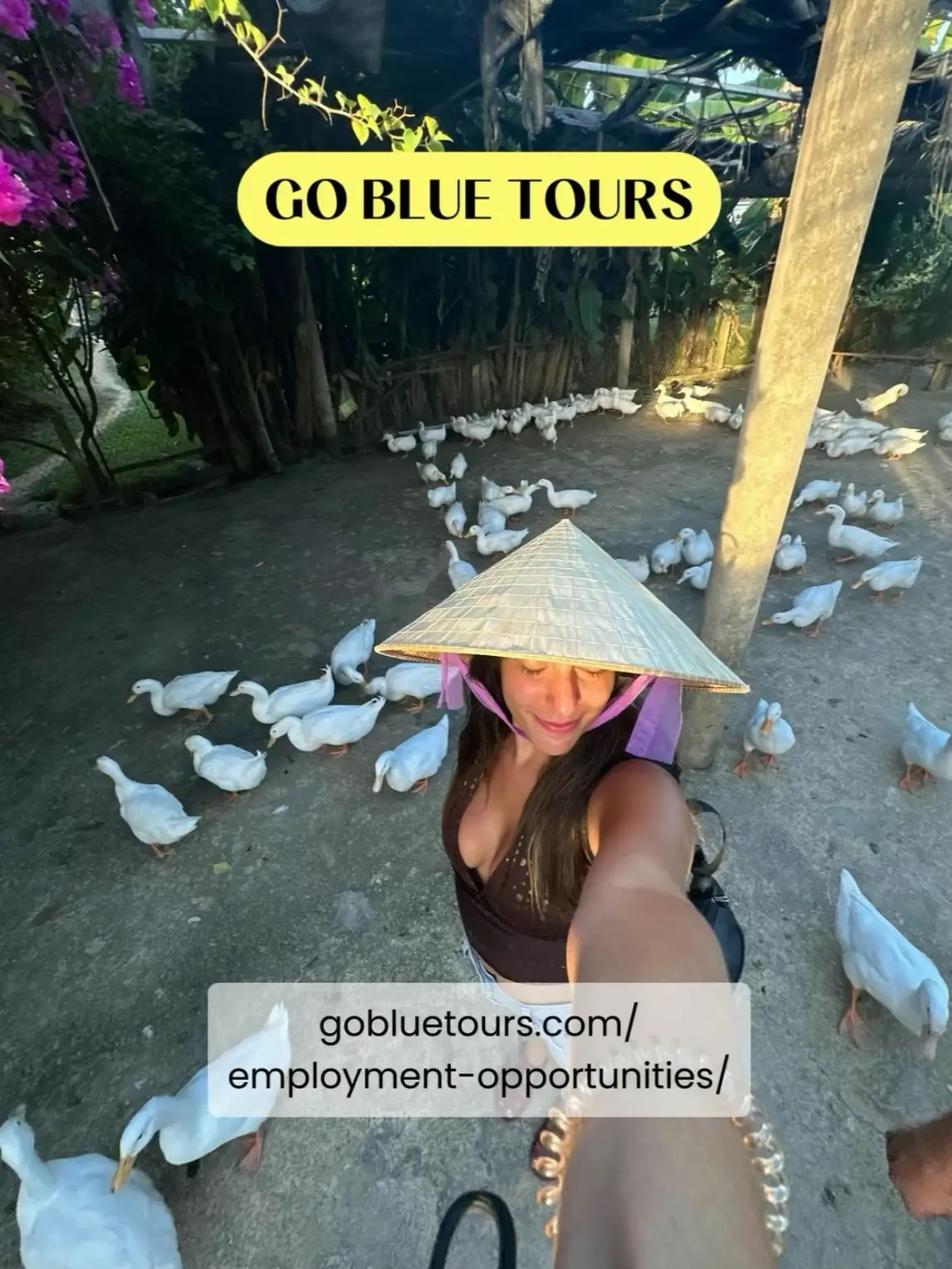  A woman wearing a blue hat and a purple shirt is standing in front of a group of birds.