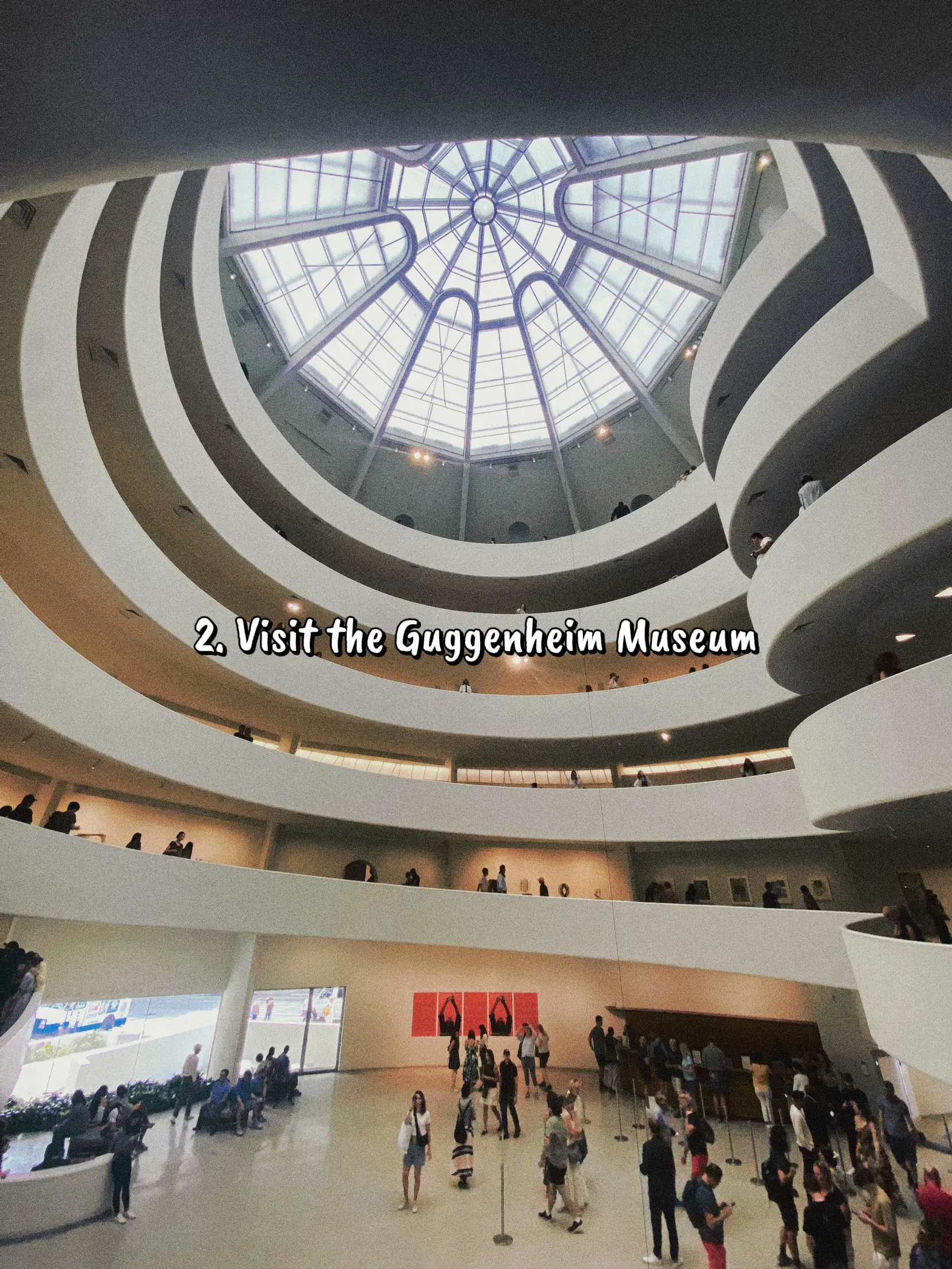  A large group of people are gathered in a building with a dome. The building has a sign that says "Visit the Guggenheim Museum".