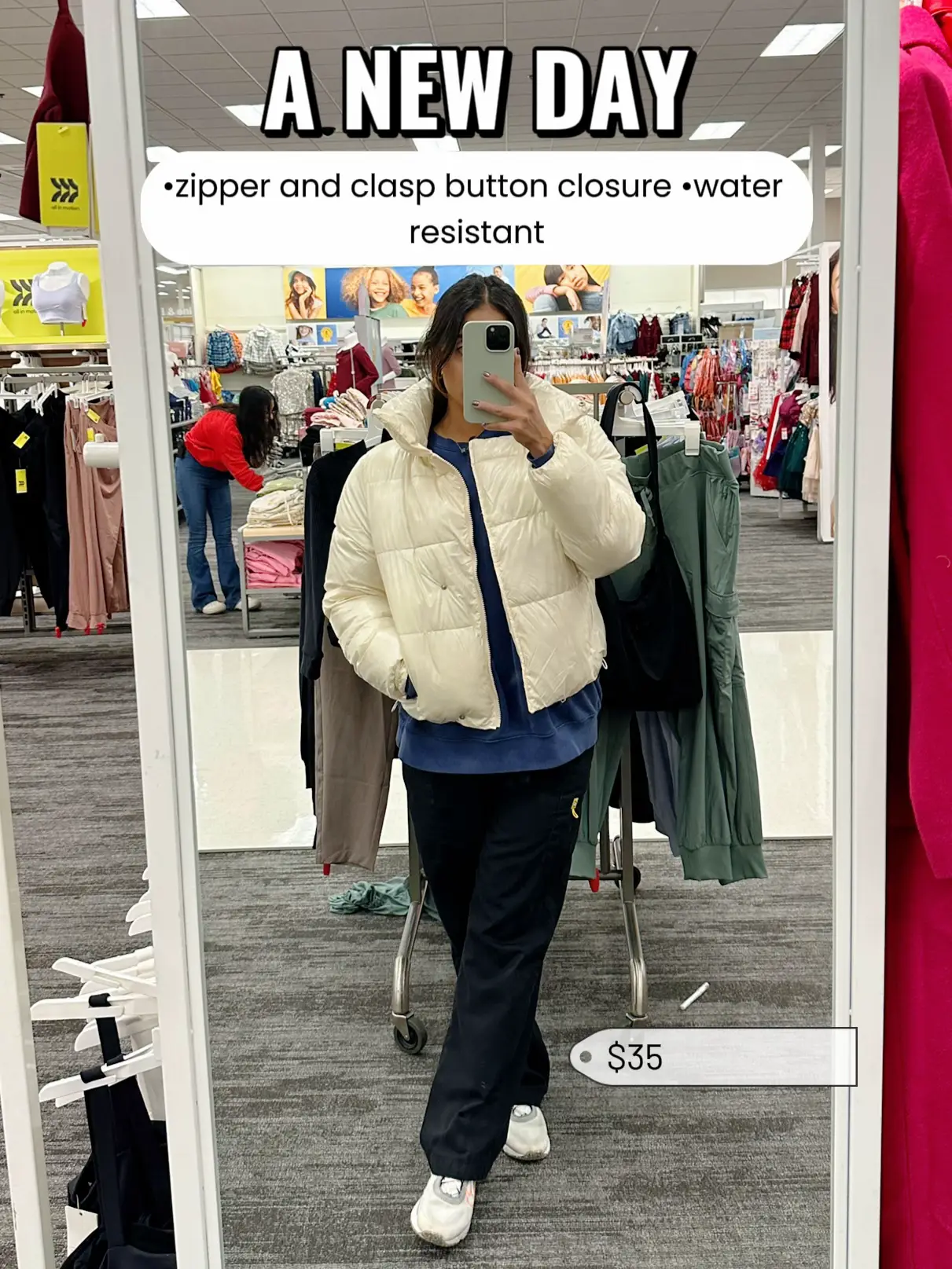  A woman in a brown jacket and grey pants is taking a selfie in a store.