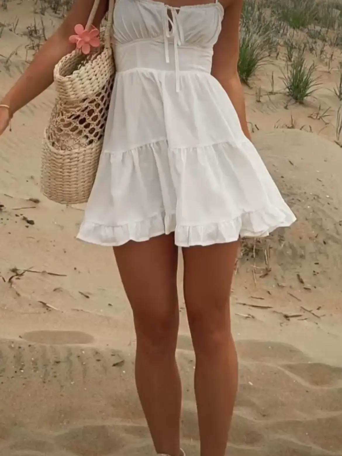  A woman wearing a white dress and white shoes is standing on a beach.