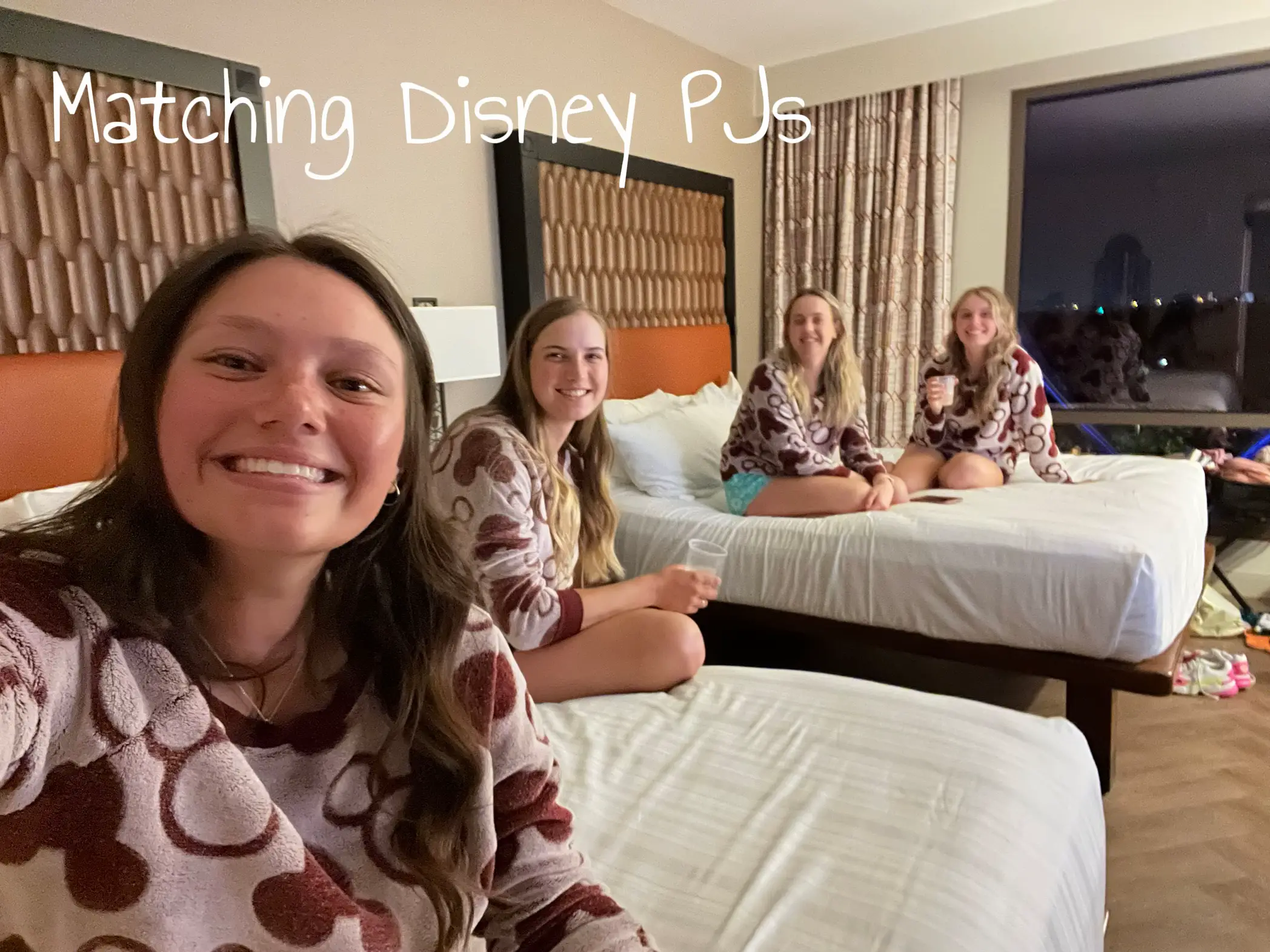  Three women are sitting on a bed wearing matching Disney PJs.