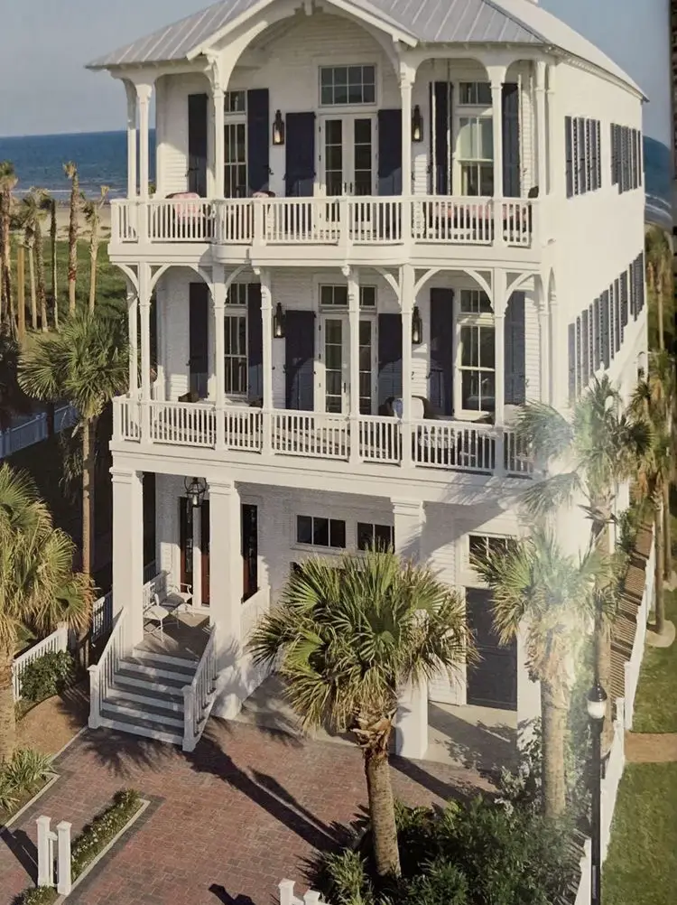  A white house with a porch and a palm tree in front of it.