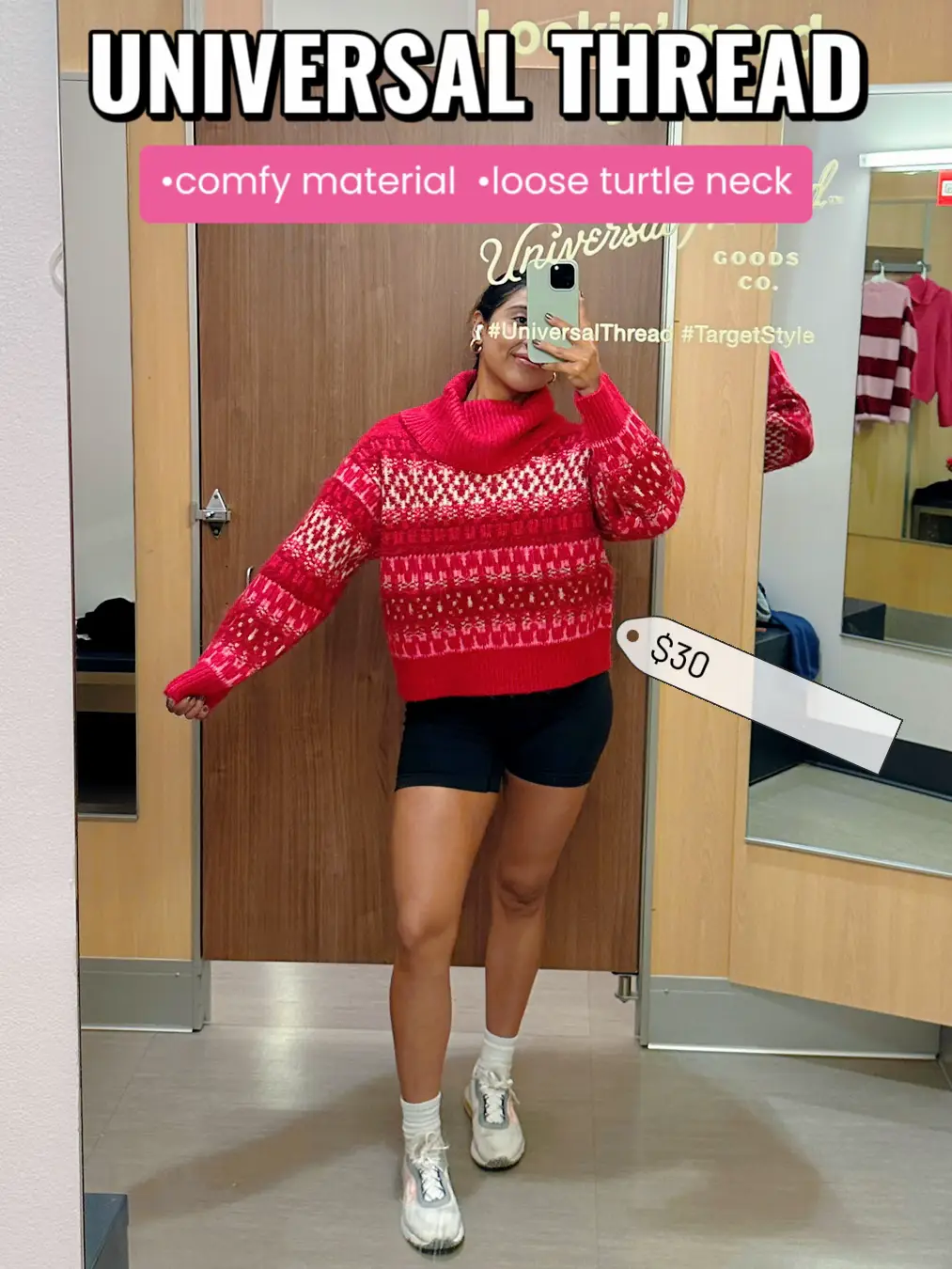  A woman in a red sweater and black shorts is taking a selfie in a mirror.