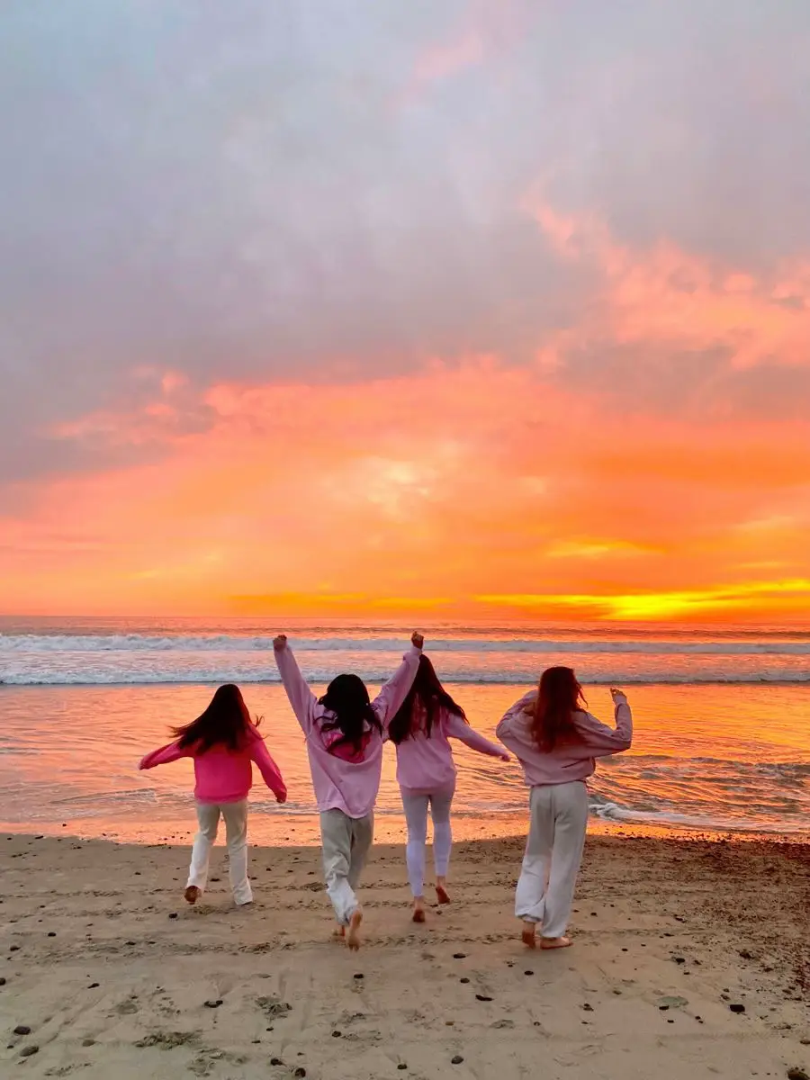  Four girls are standing on a beach, waving at the camera.