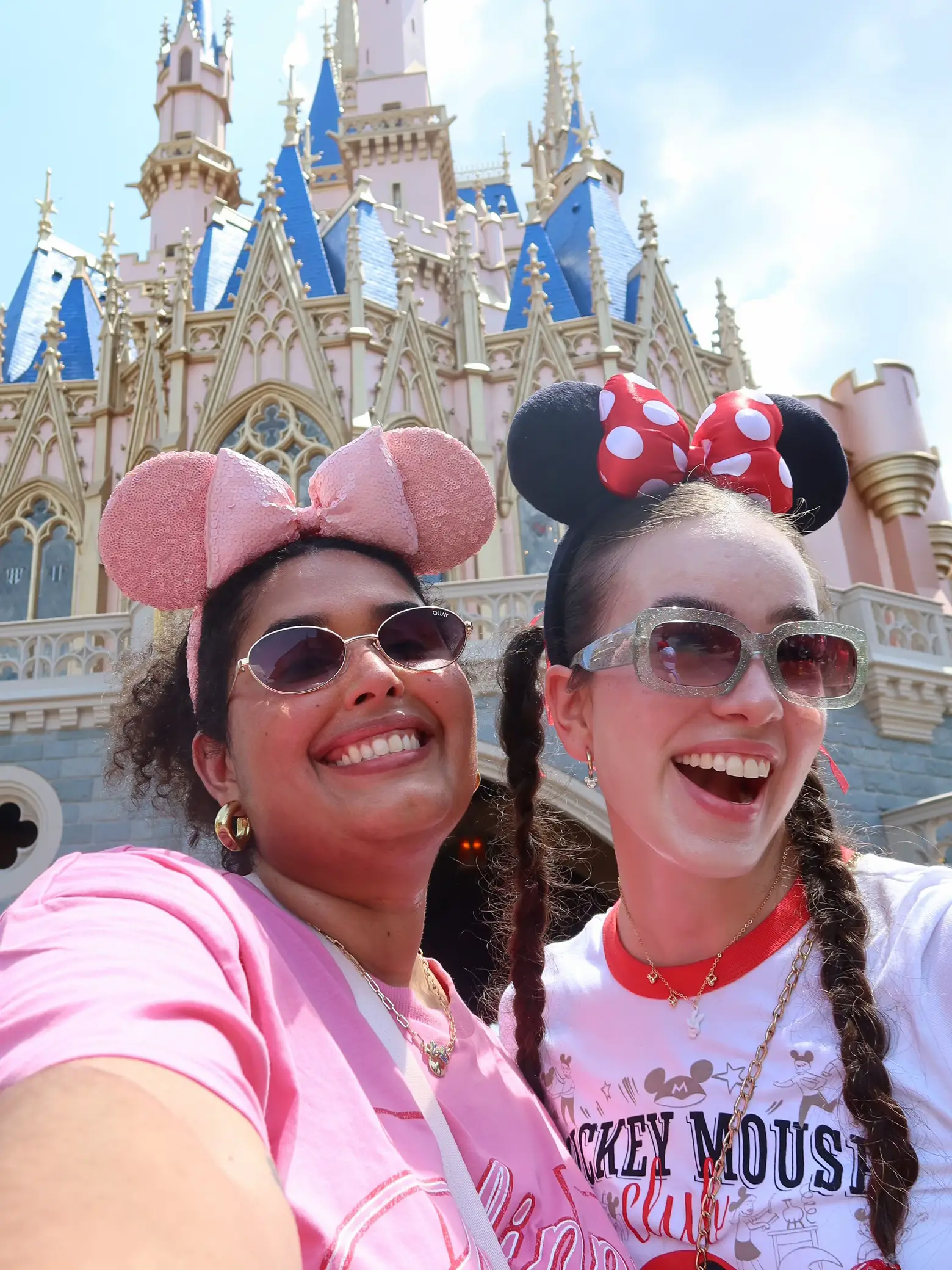  Two women are standing in front of a castle, wearing Mickey Mouse shirts. They are smiling and posing for a picture.