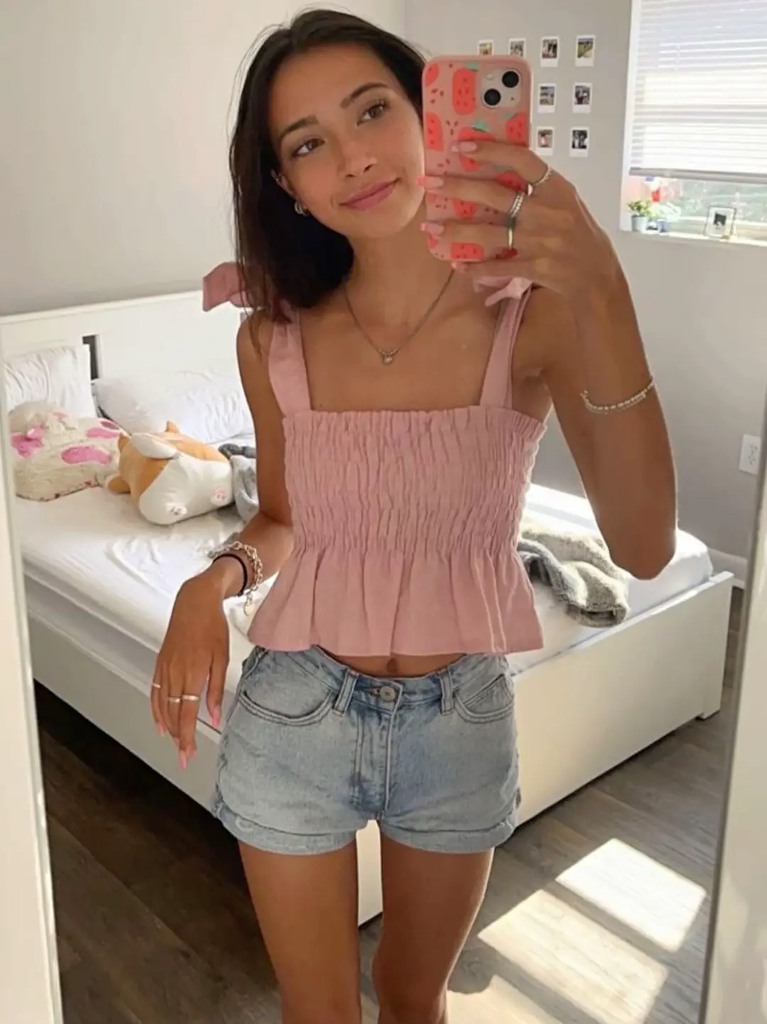  A woman in a pink shirt is taking a selfie in a mirror.