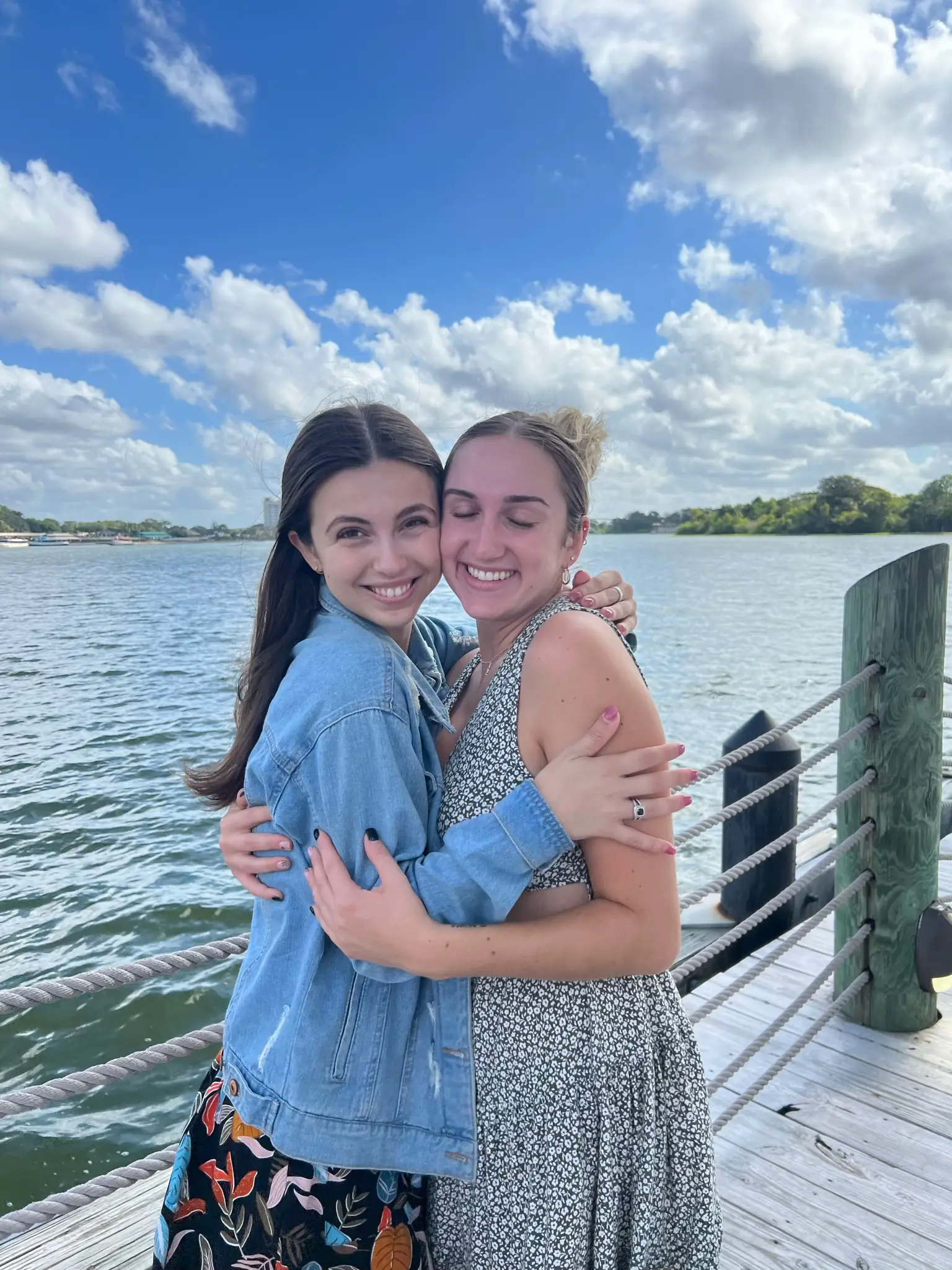  Two women are hugging each other on a pier overlooking the ocean.