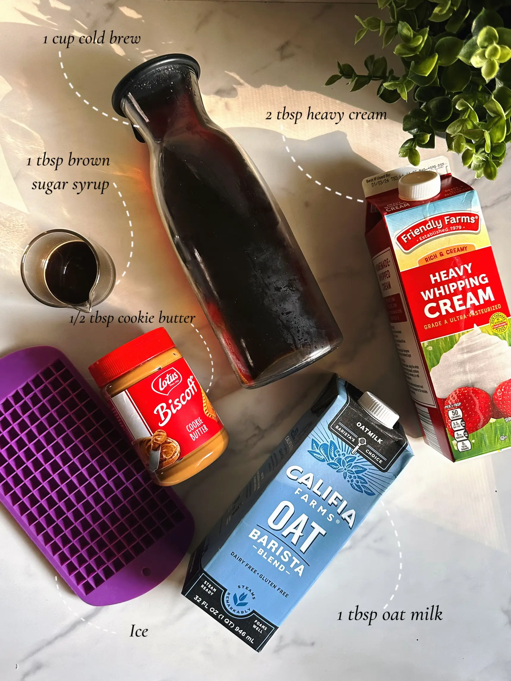  A bottle of oat milk, a carton of heavy whipping cream, a bottle of brown sugar syrup and a cup of cold brew are placed on a table.