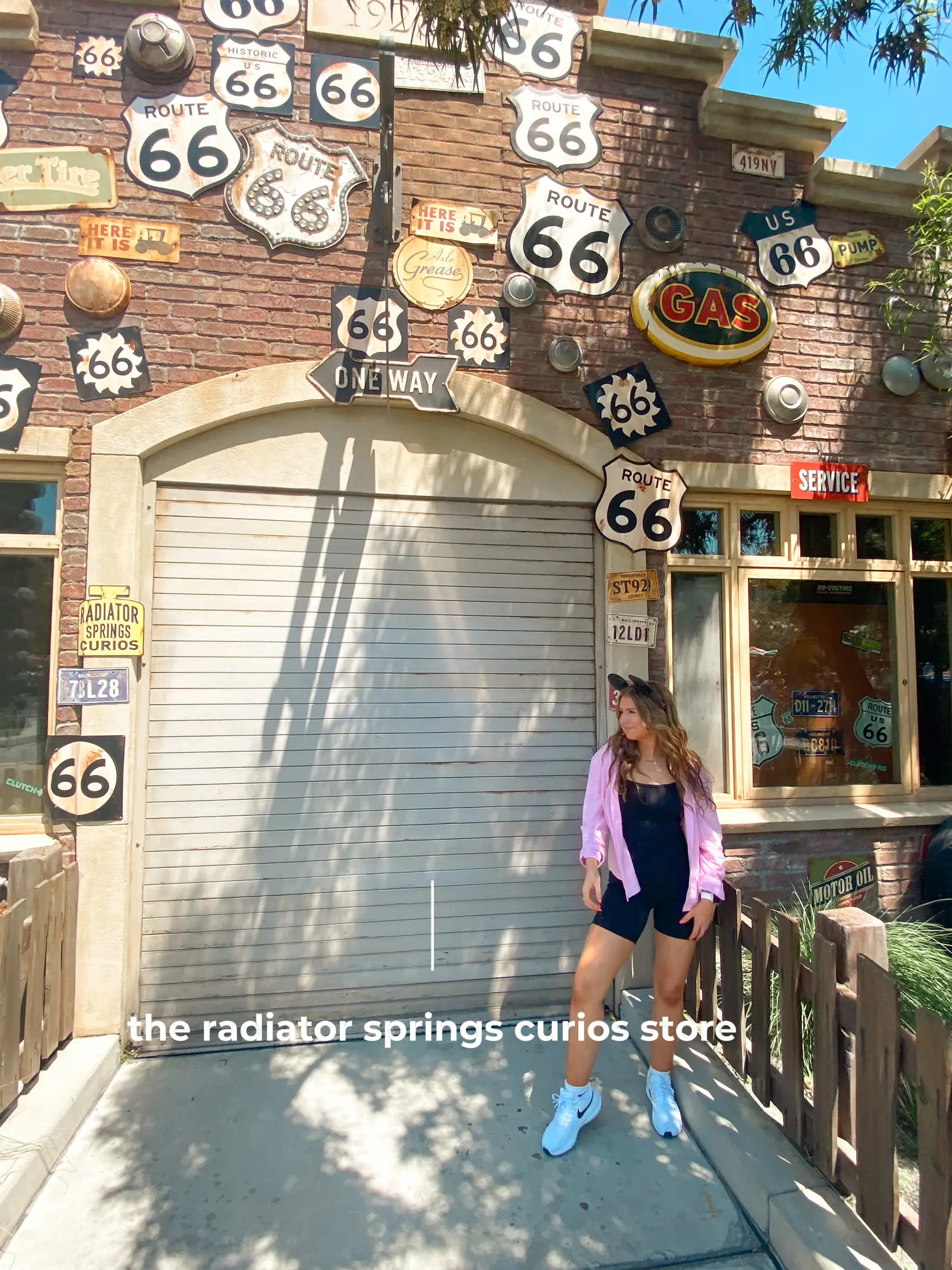 A woman is standing in front of a store with a sign that says " Route 66". The store has a variety of signs on the door, including a " Route 66" sign.