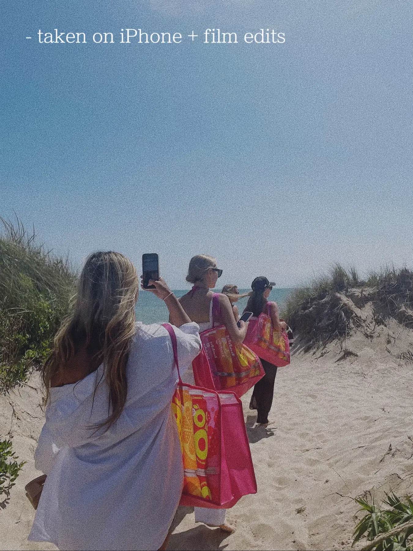  A group of people are walking on a beach, with some of them holding bags. One person is taking a selfie with the others in the background.