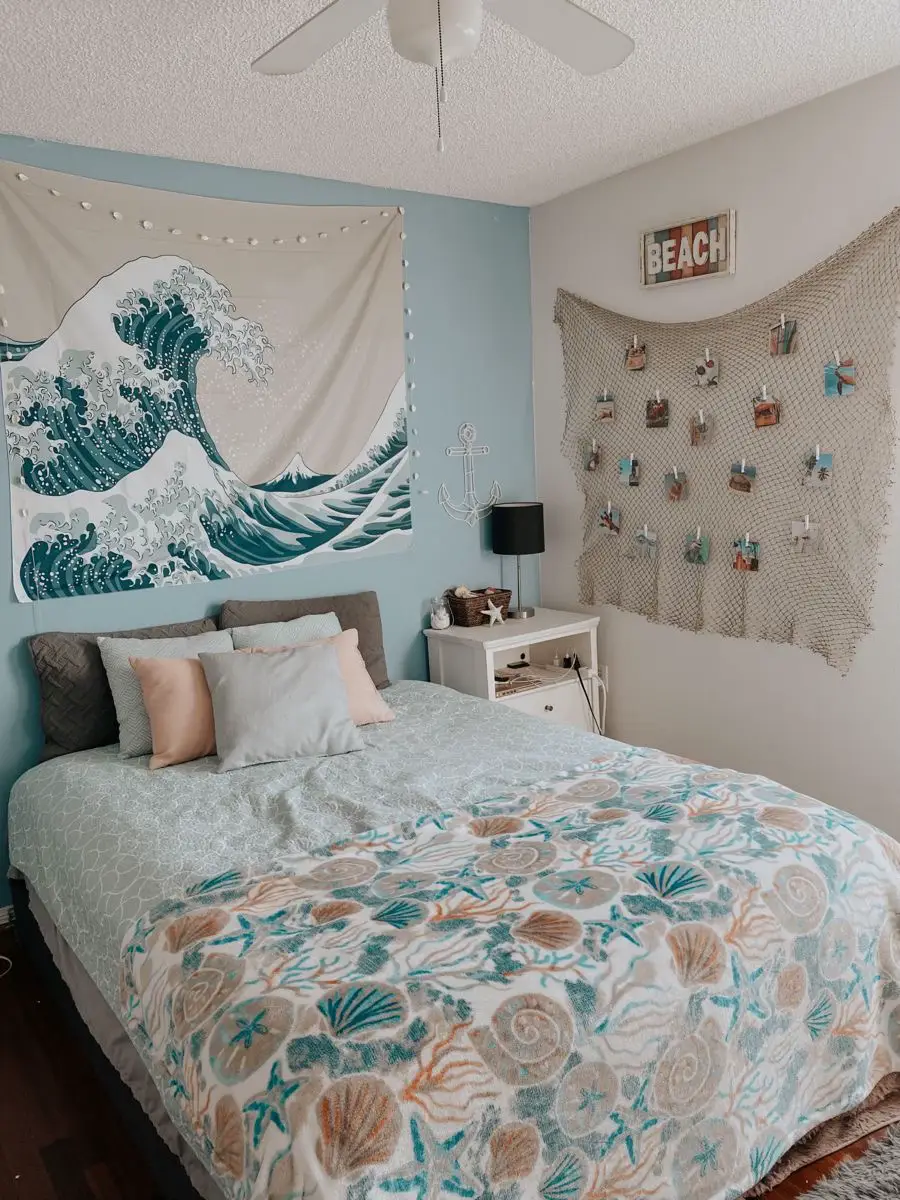  A bedroom with a bed with a yellow and white comforter and a white pillow. The room is decorated with a surfboard on the wall and a picture of a wave on the wall.