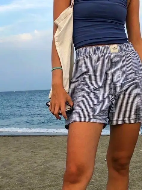  A woman wearing a blue top and white shorts is standing on a beach.