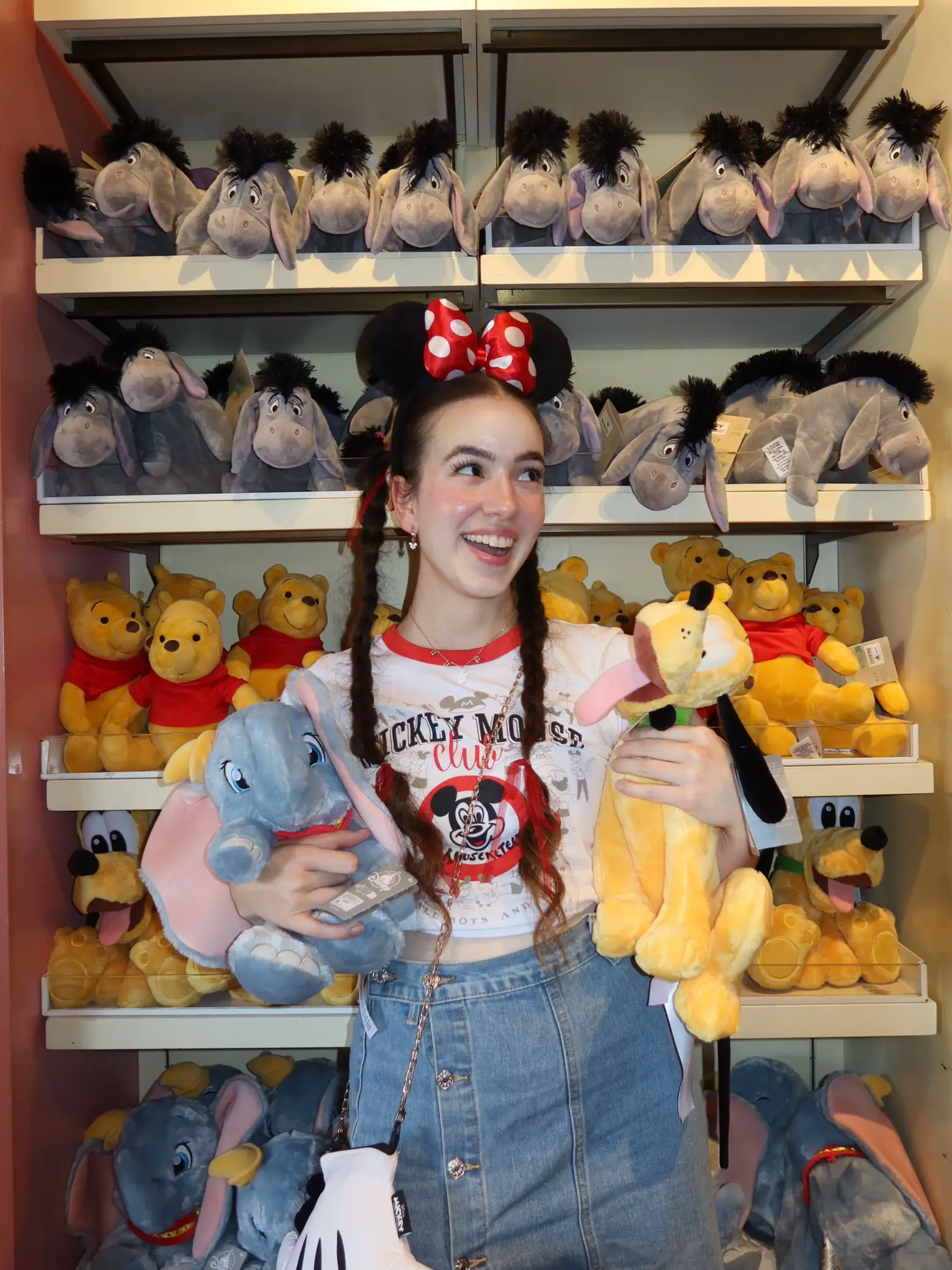  A woman wearing a blue shirt and jeans is standing in front of a display of stuffed animals. She is holding a frisbee and appears to be enjoying her time with the toys.